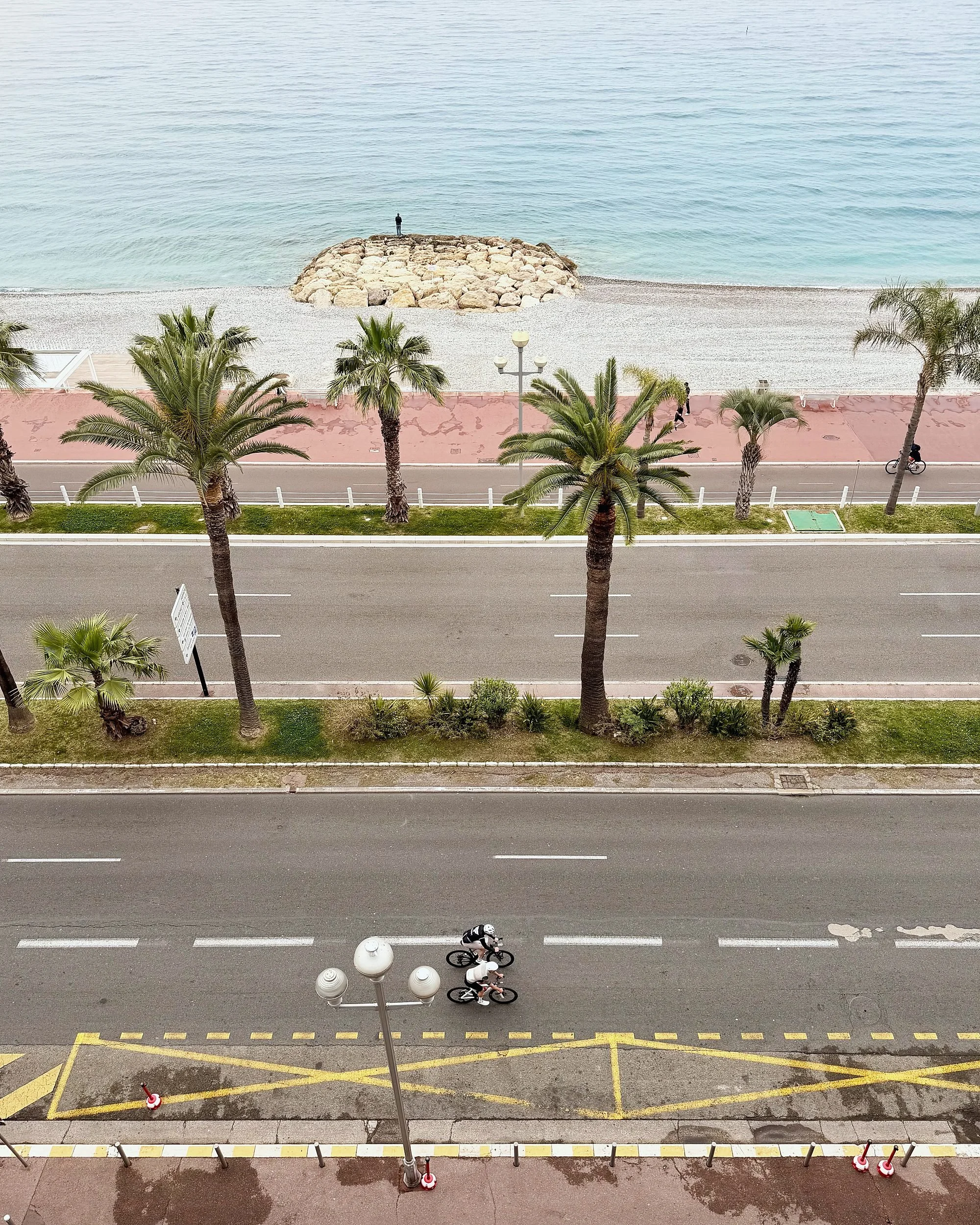 High-angle daytime view of the Promenade des Anglais, palms, pebble beach and sea
