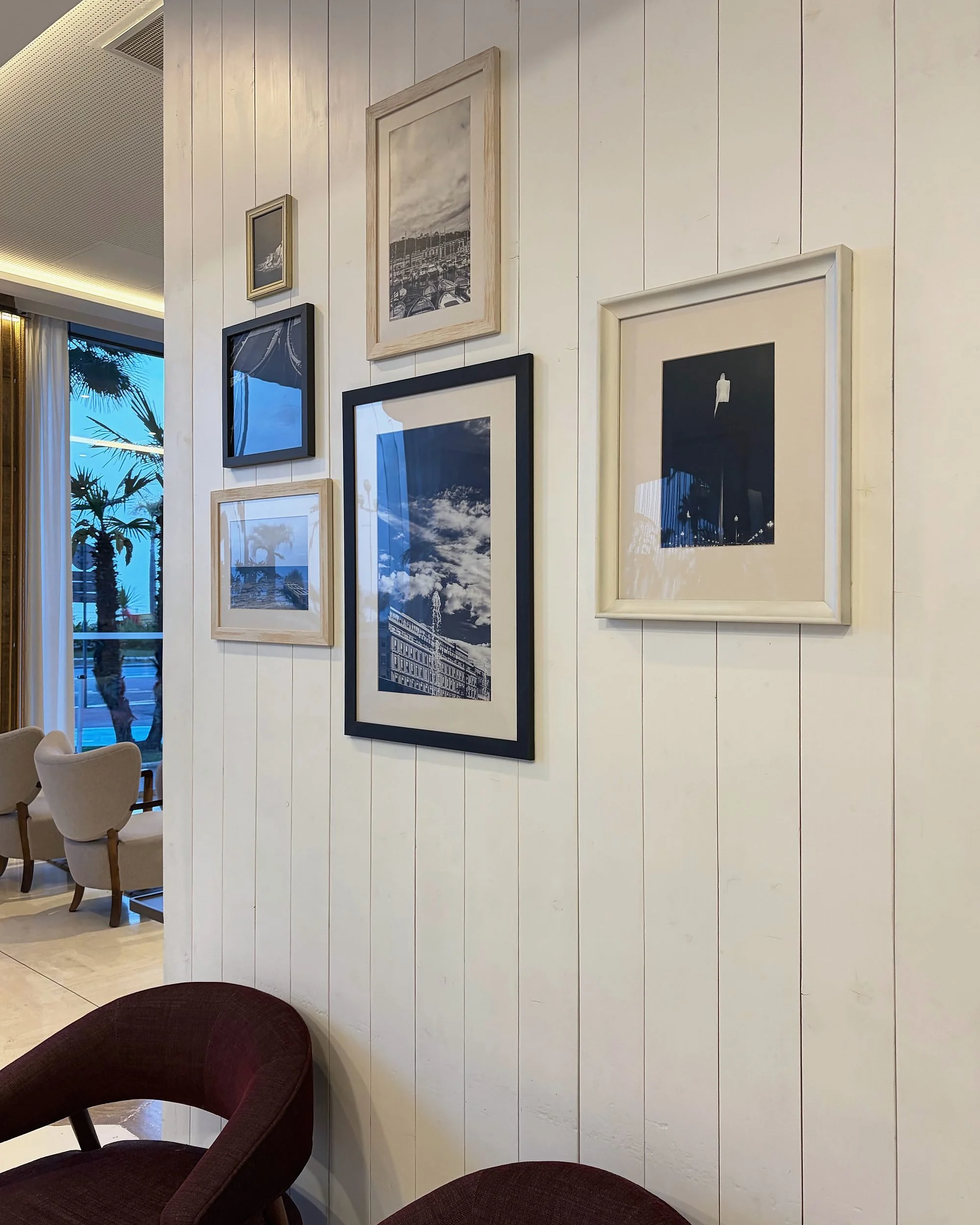 Cream wood-panelled lobby wall with a gallery of framed photographs and burgundy chairs