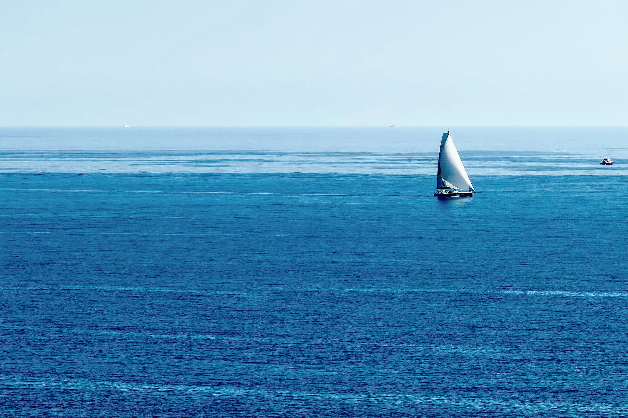 Single white sailboat on open blue sea under a pale sky