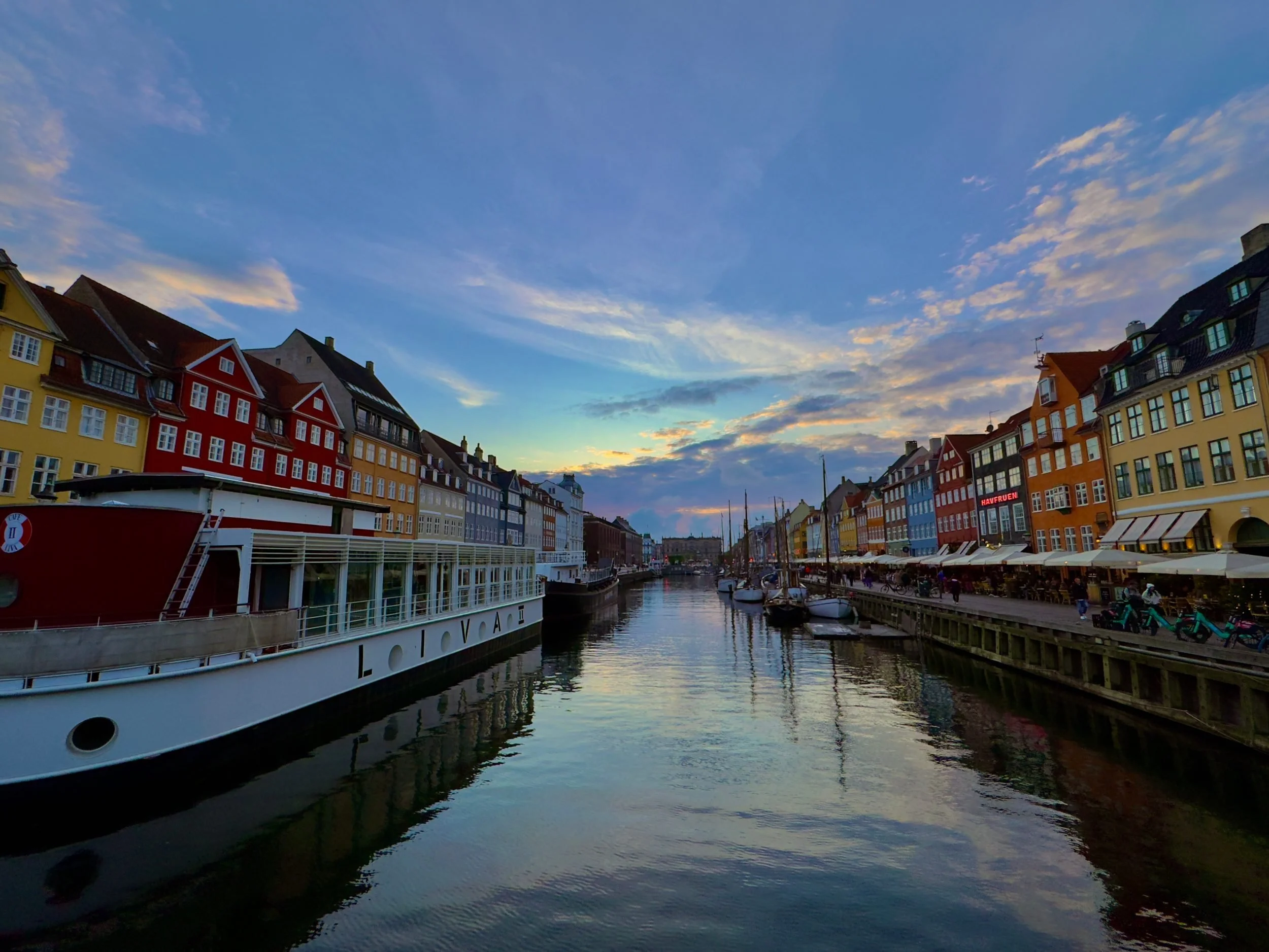Nyhavn canal at dusk, boats moored beside lit waterfront houses.