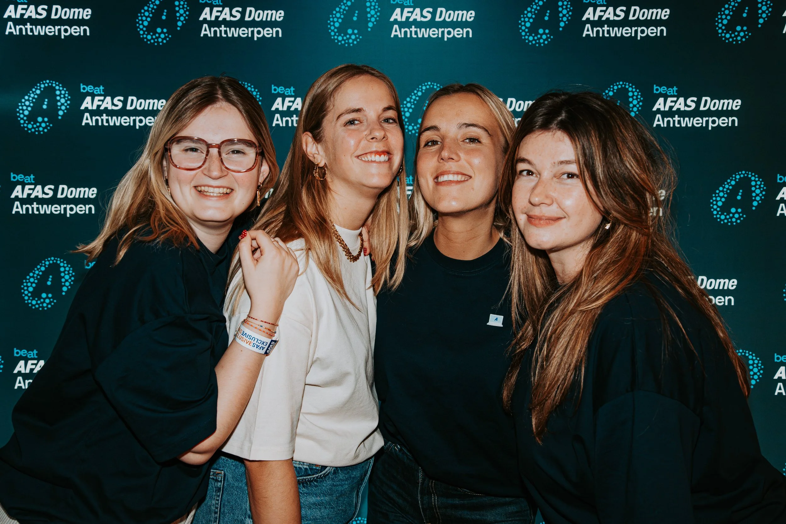 Four young women smiling and posing together at a event with a backdrop that says 'beat AFAS Dome Antwerpen'.