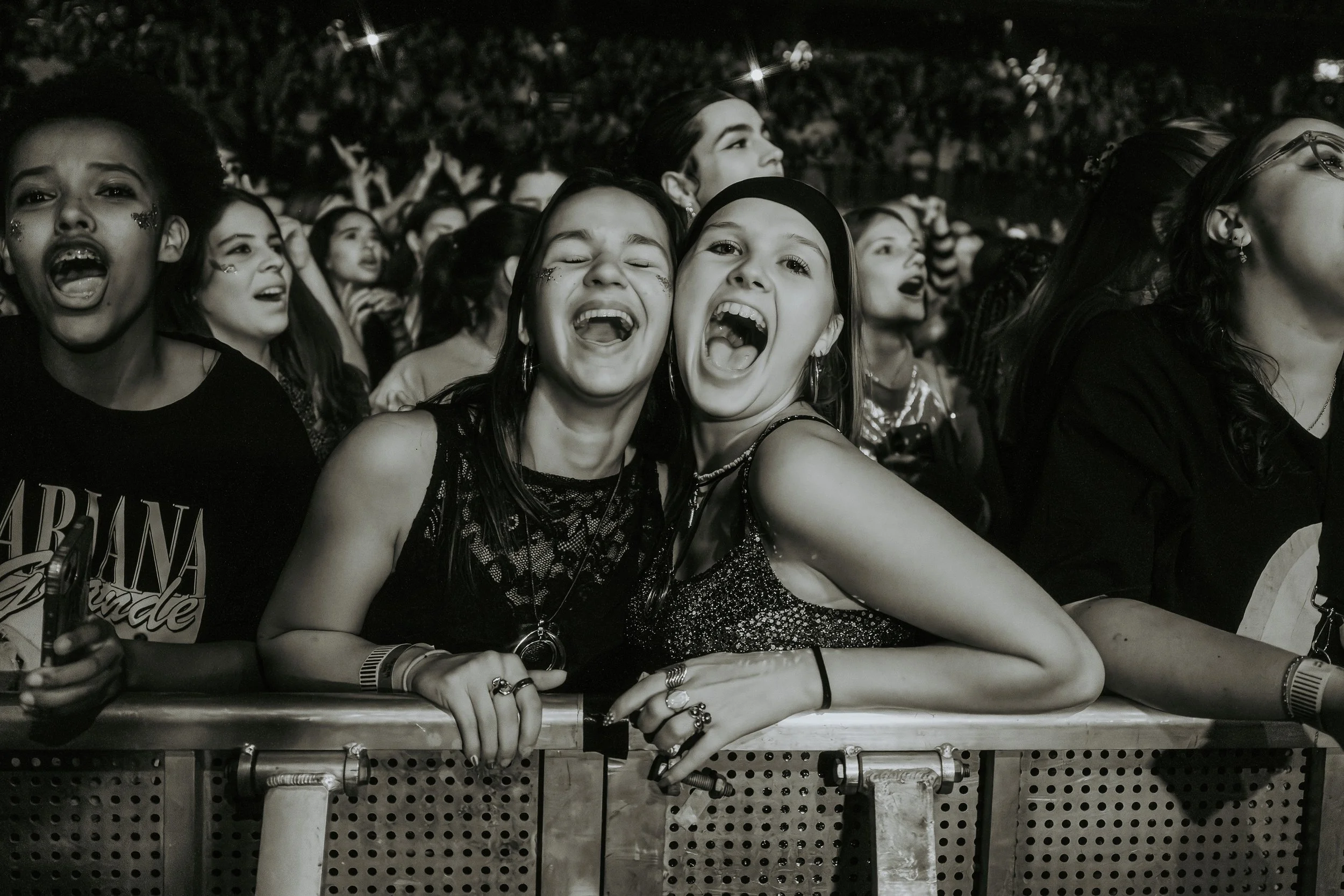 A group of excited young women at a concert, front-row view; some are singing or shouting, with joyful expressions.
