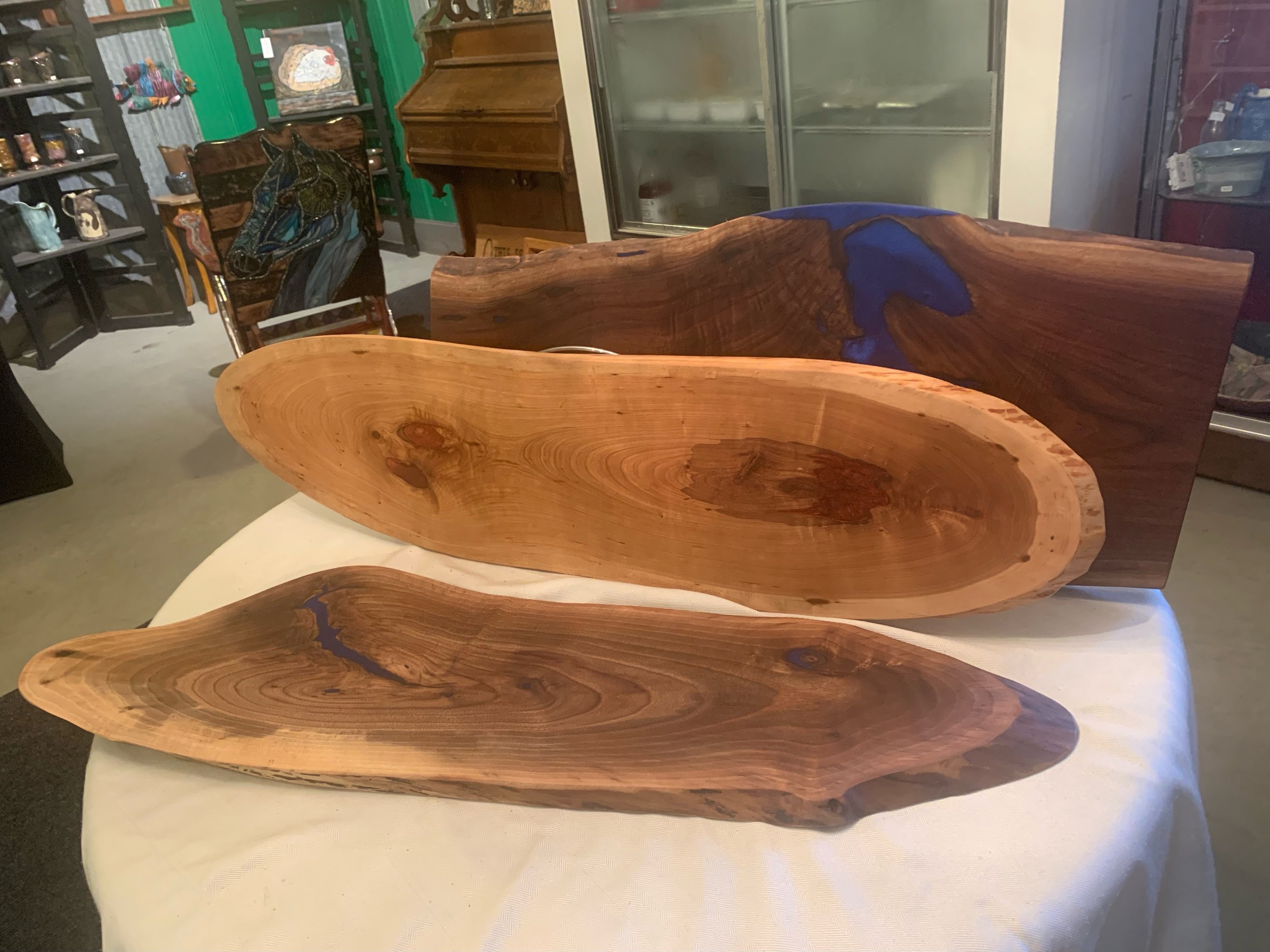 Three wooden bowls with natural grain patterns and blue resin accents displayed on a table at a store.