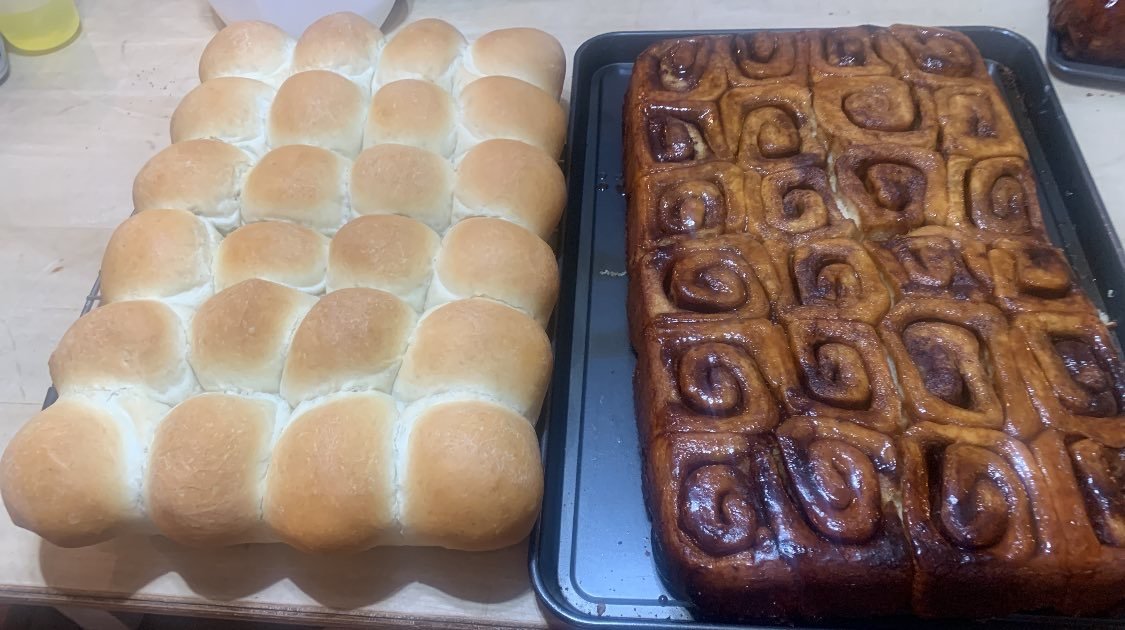 Tray of freshly baked dinner rolls and a large tray of cinnamon rolls with icing.