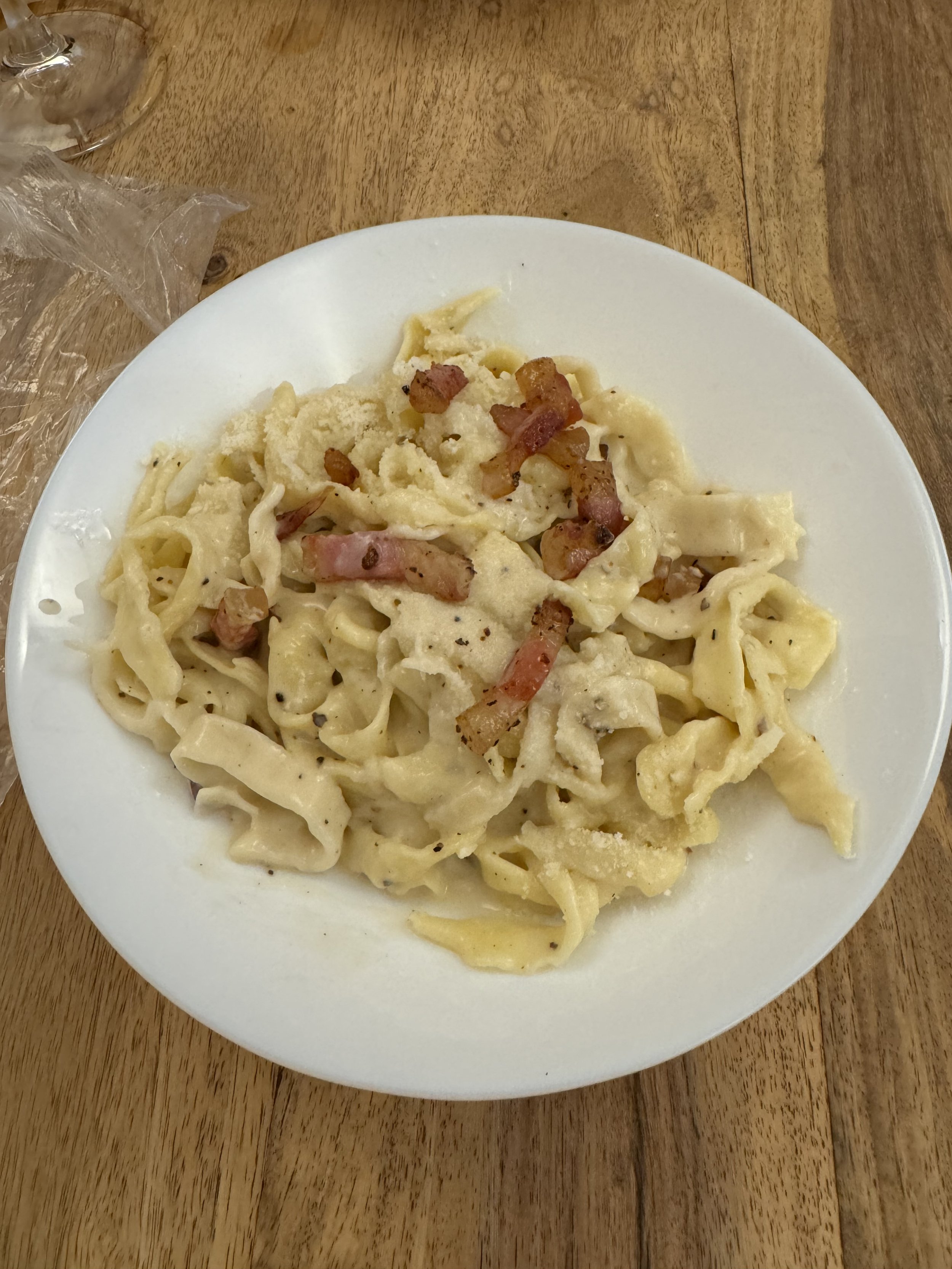 Plate of creamy fettuccine alfredo with bacon bits on a wooden table.