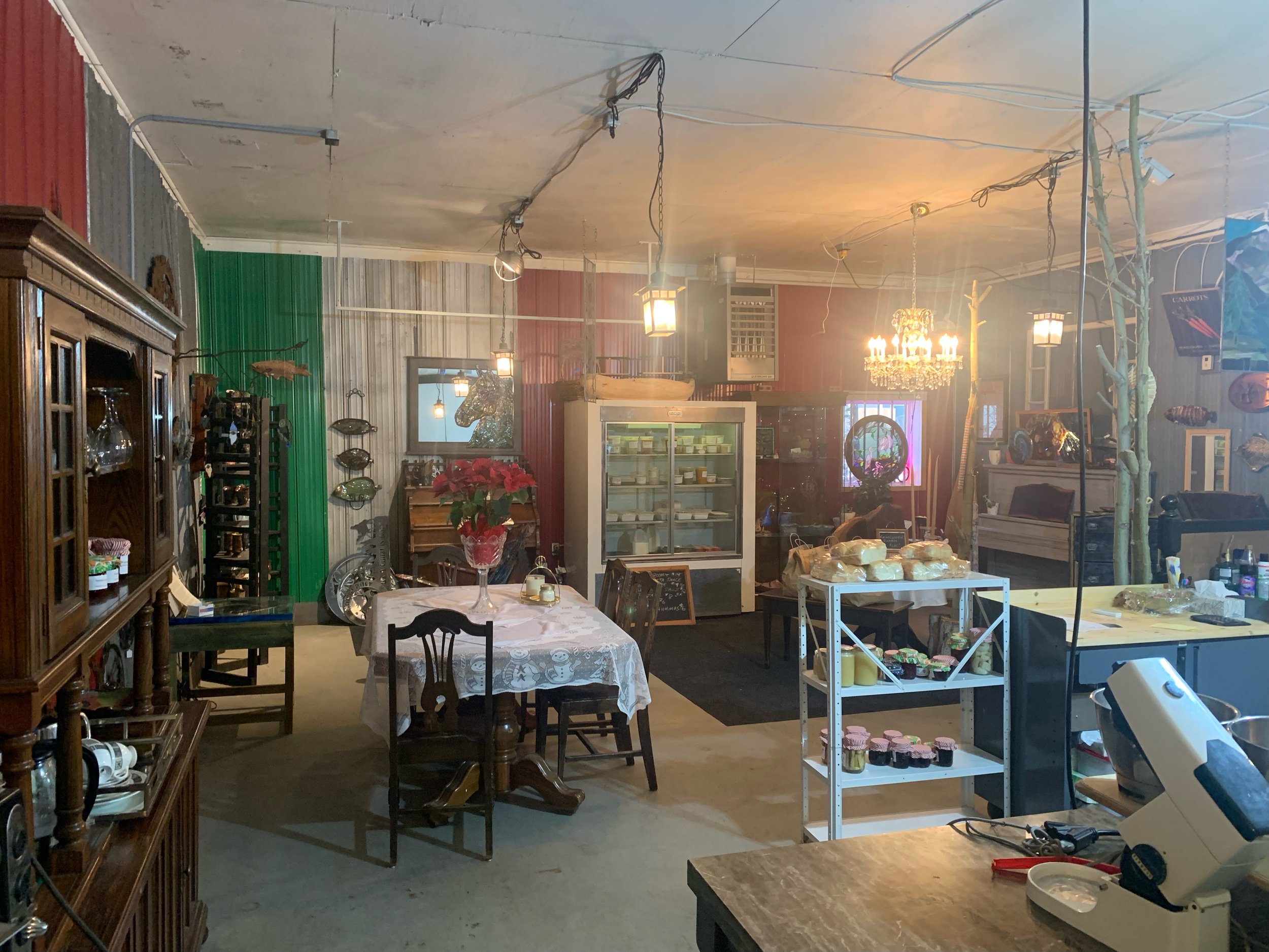 Indoor space with a dining table, shelves, decorated walls, and various items and fixtures, including a chandelier and food display.
