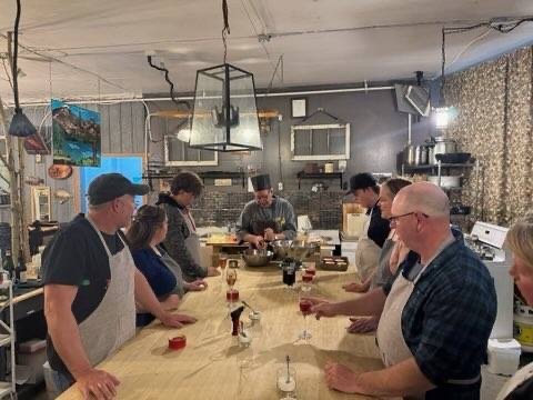 People participating in a cooking class or workshop around a wooden counter with chef instructors and ingredients.
