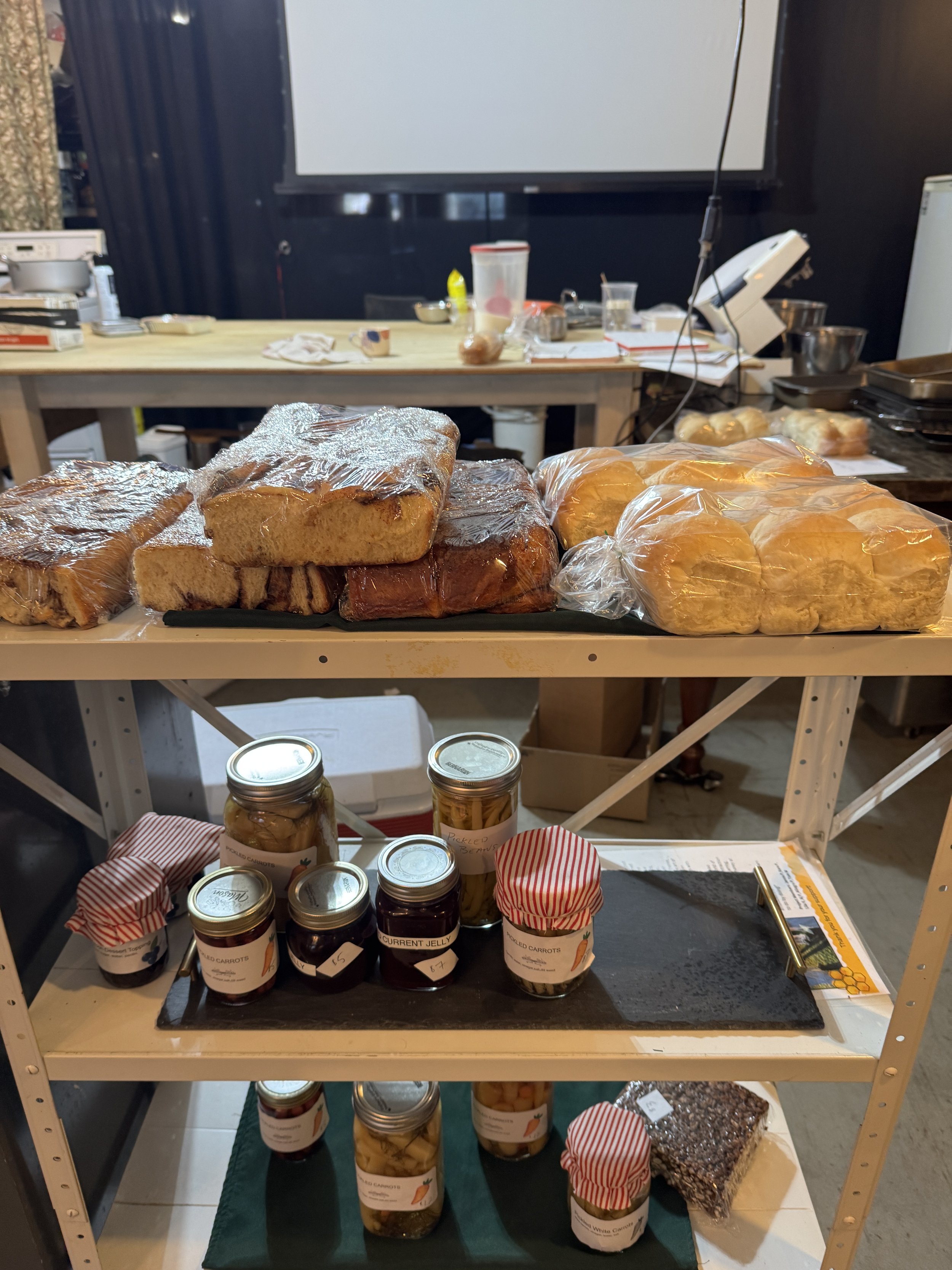 Shelf with packaged bread and jars of preserved food, in a kitchen or bakery setting.