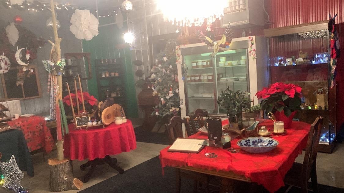 Decorated indoor space with Christmas and holiday decor, including a Christmas tree, poinsettias, butterfly ornaments, and festive table settings with red tablecloths.