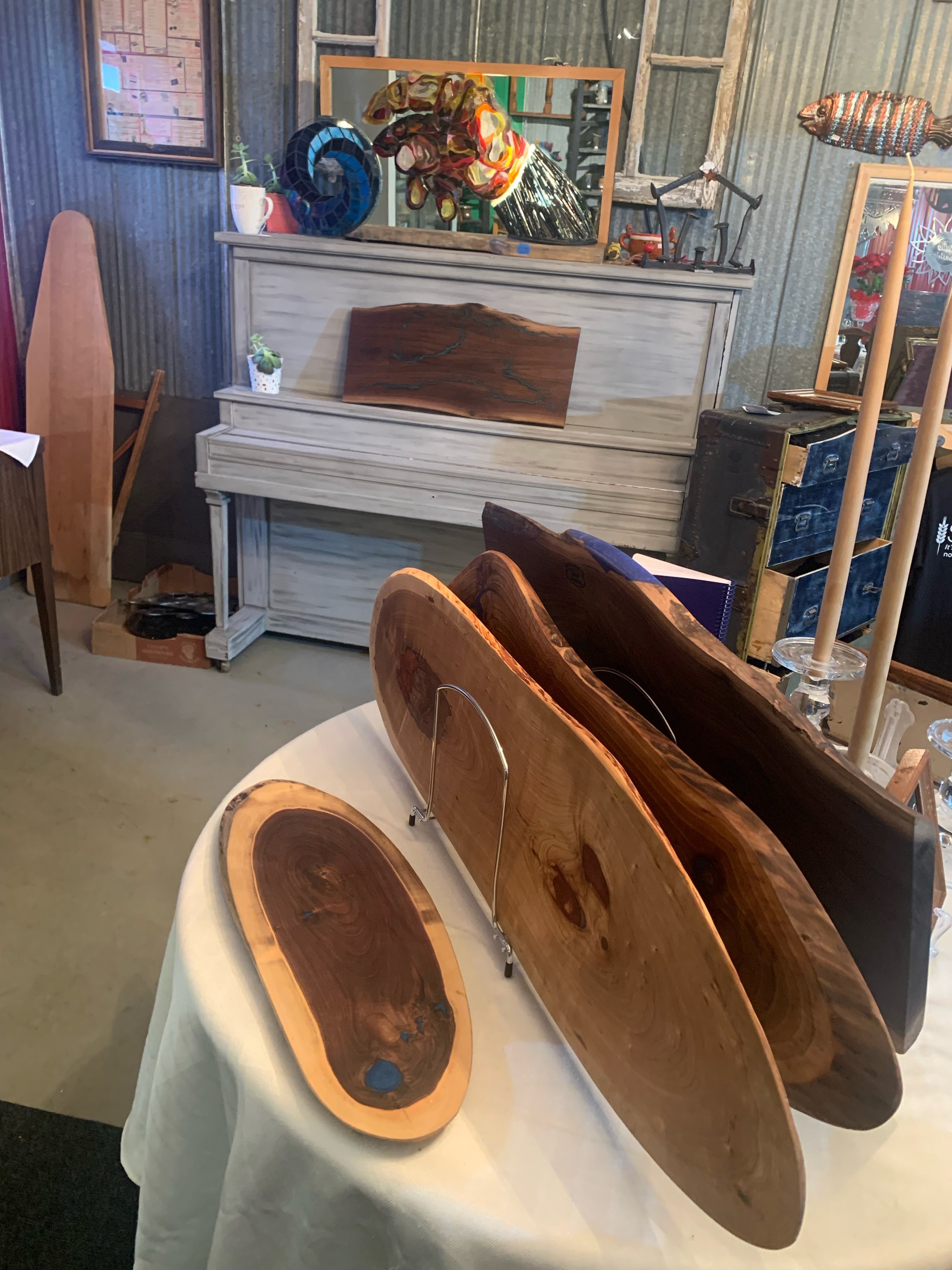 Various wooden art pieces displayed on a table, with some standing and others lying flat, in a rustic indoor setting.