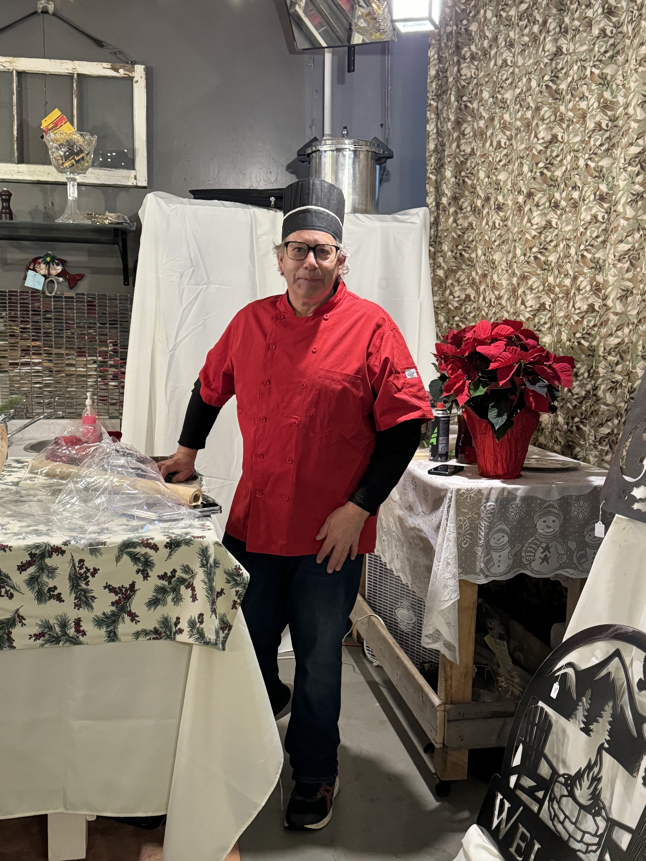 A chef wearing a red uniform and black hat standing in a decorated kitchen with a Christmas theme.
