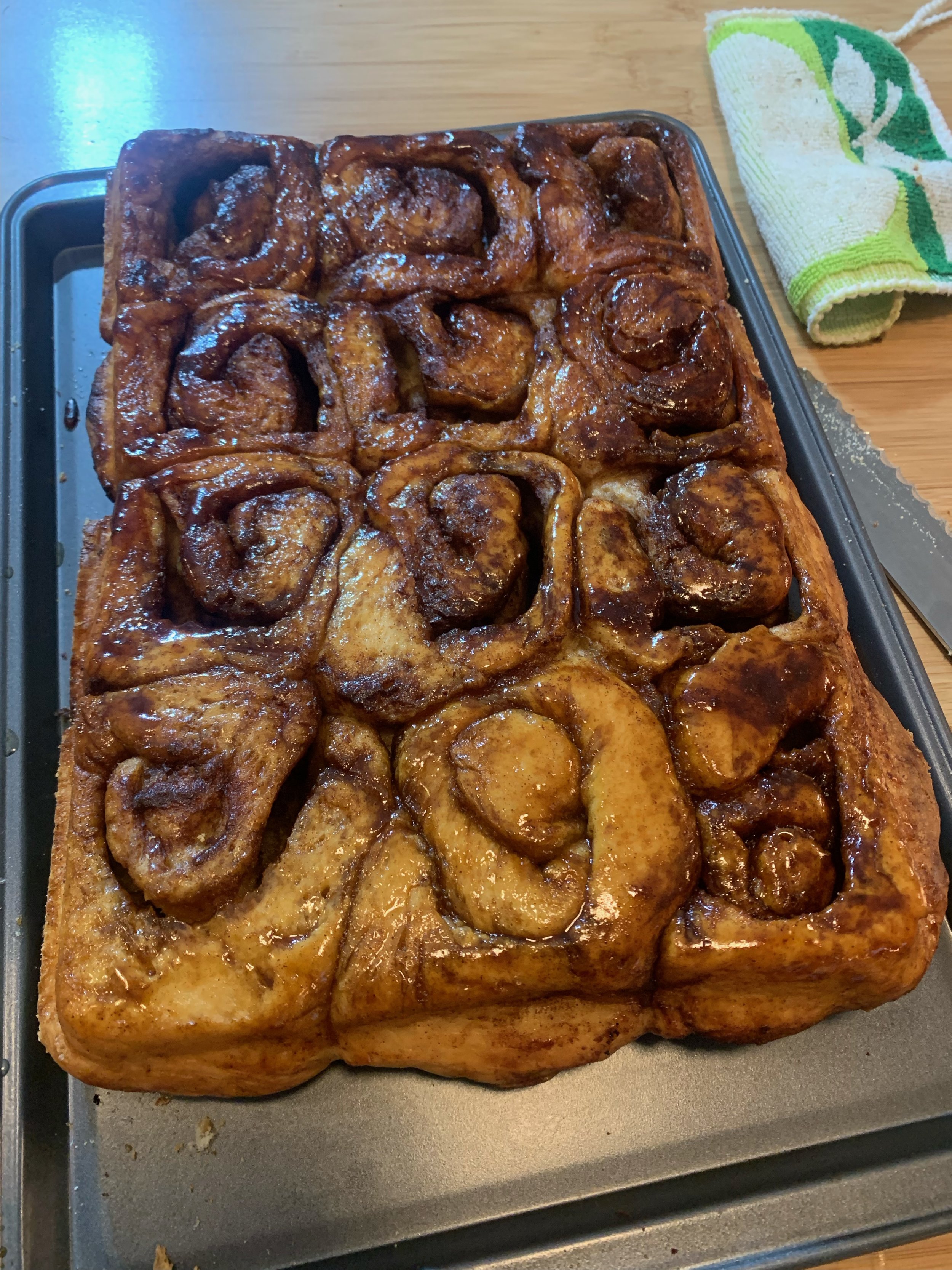 A large rectangular tray of cinnamon rolls glazed with icing.