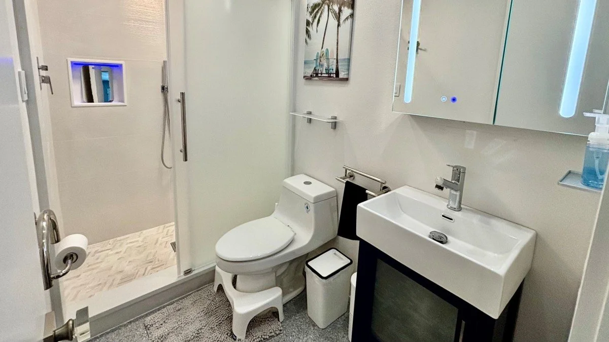 Bathroom with a shower, toilet, and small sink with illuminated mirror
