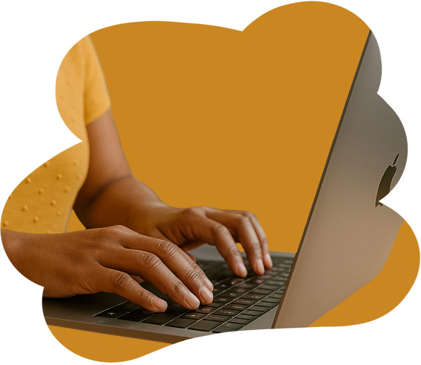 Close-up of a person's hands typing on a laptop keyboard against a mustard yellow background.