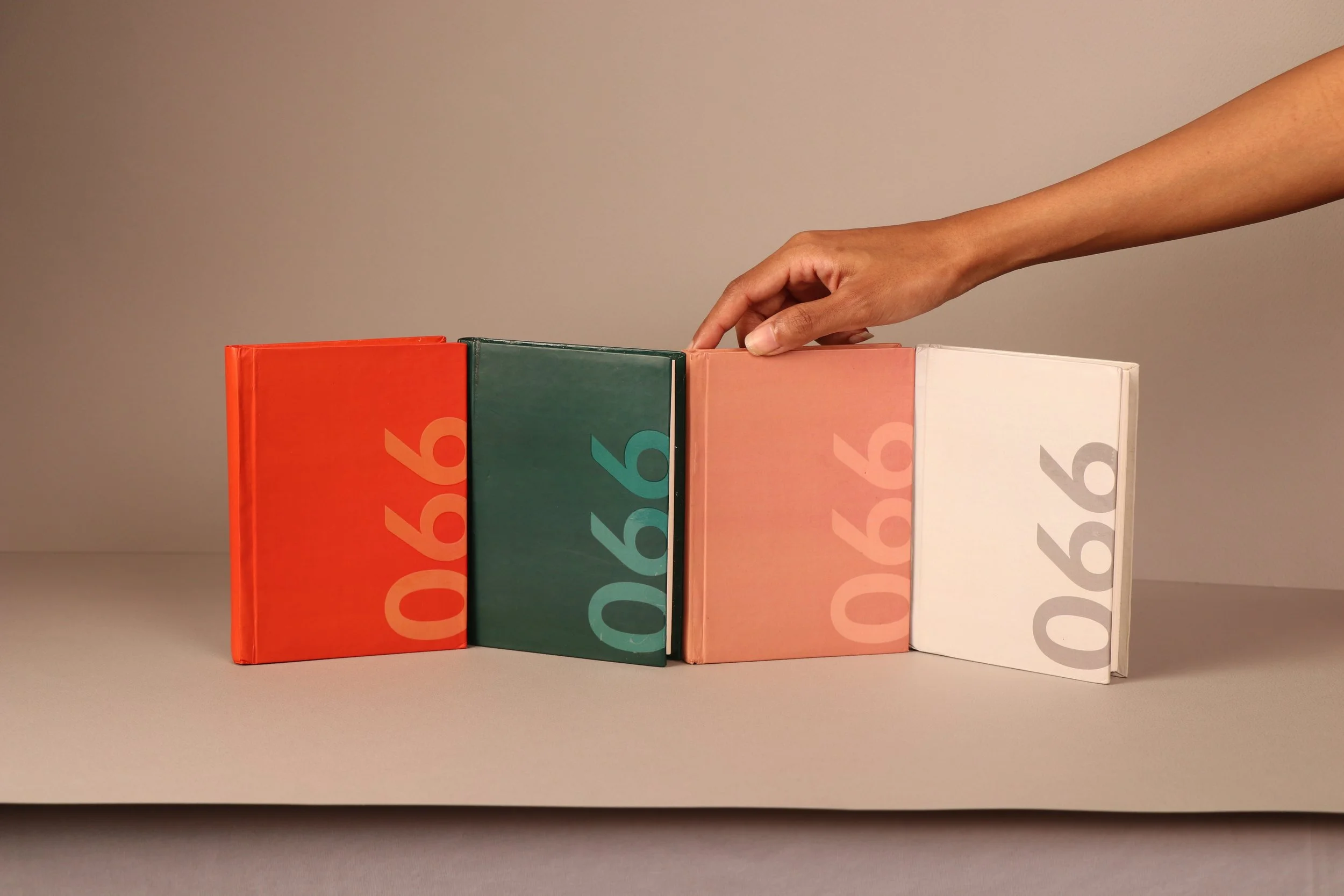 A hand placing a book on top of a row of four colorful books on a plain surface