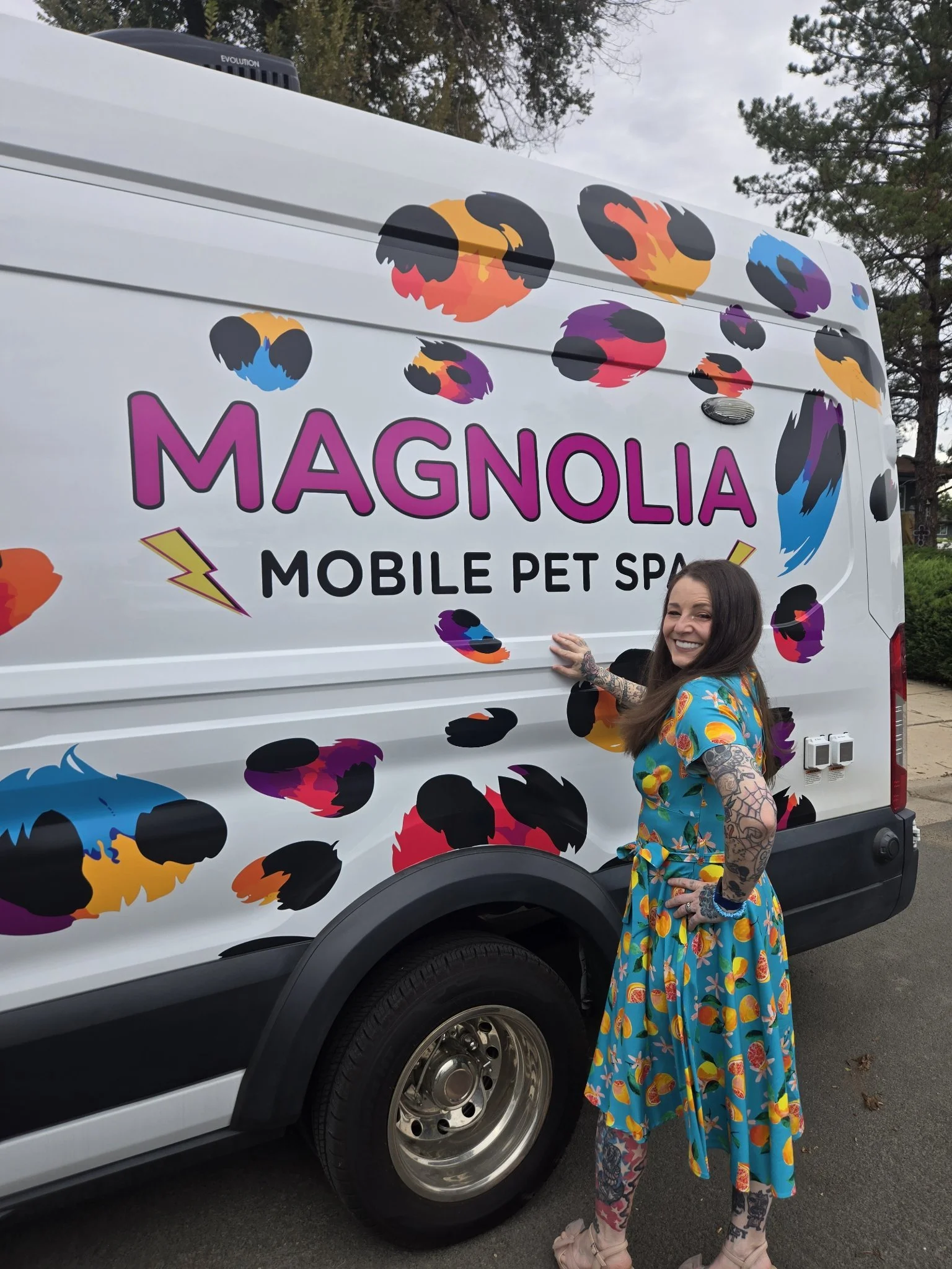 Kate in a blue dress standing beside the leopard-print Magnolia mobile pet spa van