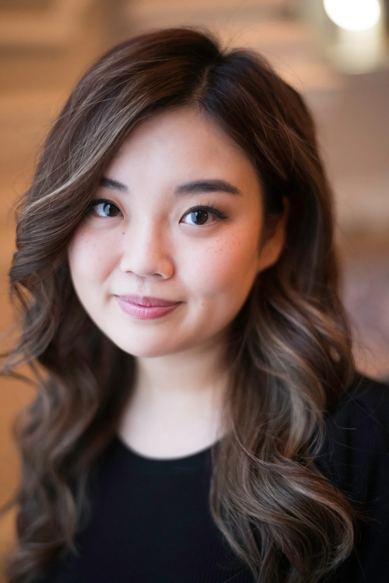 Close-up of a young woman with wavy brown hair and a subtle smile, wearing a black top.