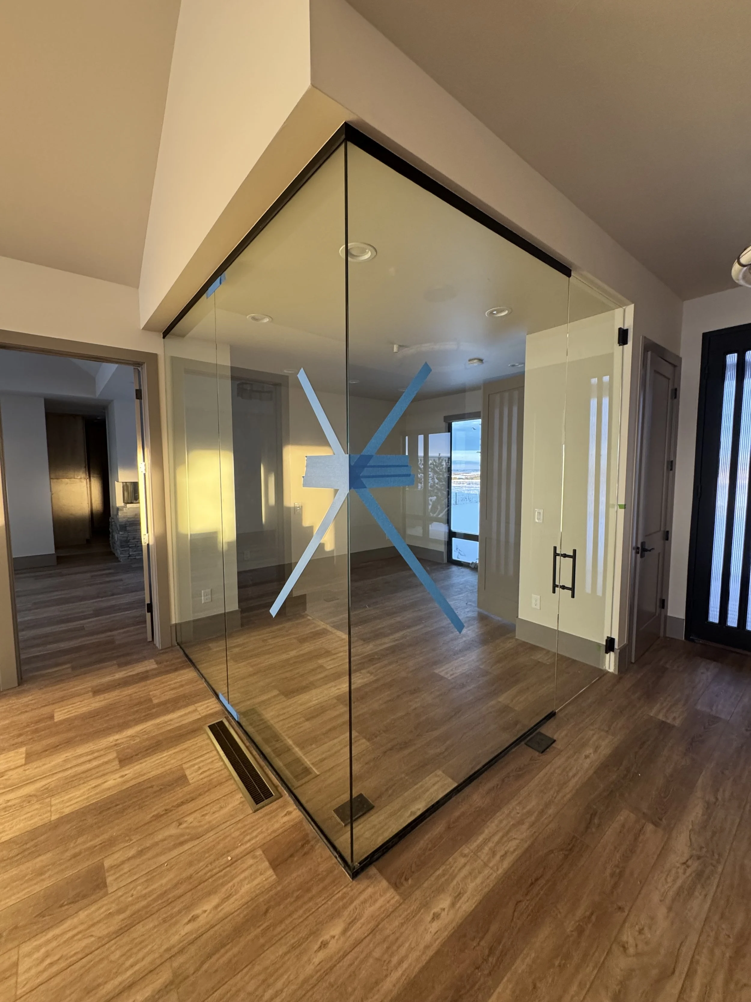A glass-walled room with a large blue clock design on the glass, located in a modern home with wood flooring and large windows showing a view outside.