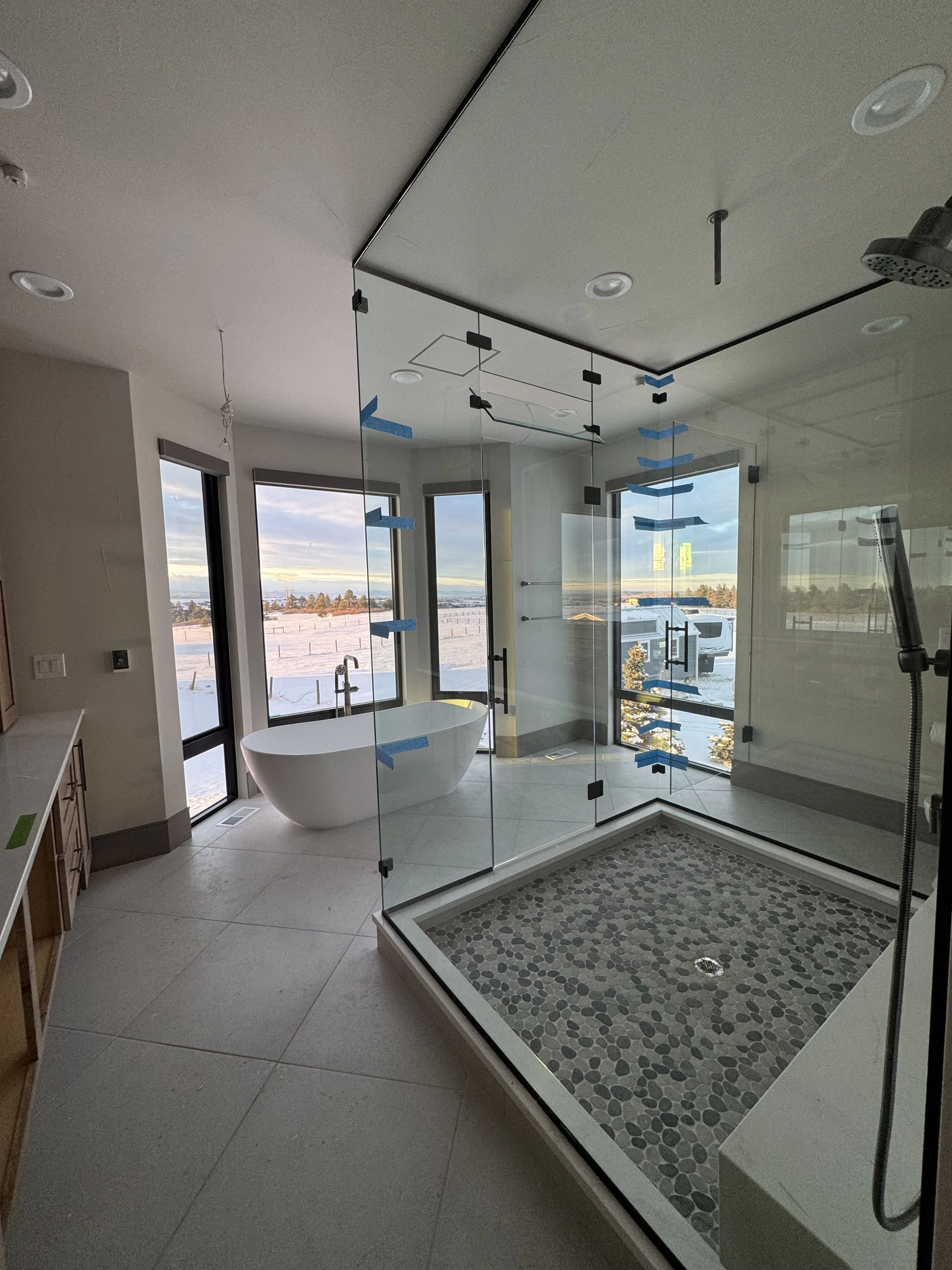Modern bathroom with a freestanding bathtub, large windows with a snowy outdoor scene, and a glass-enclosed shower with pebble stone floor.