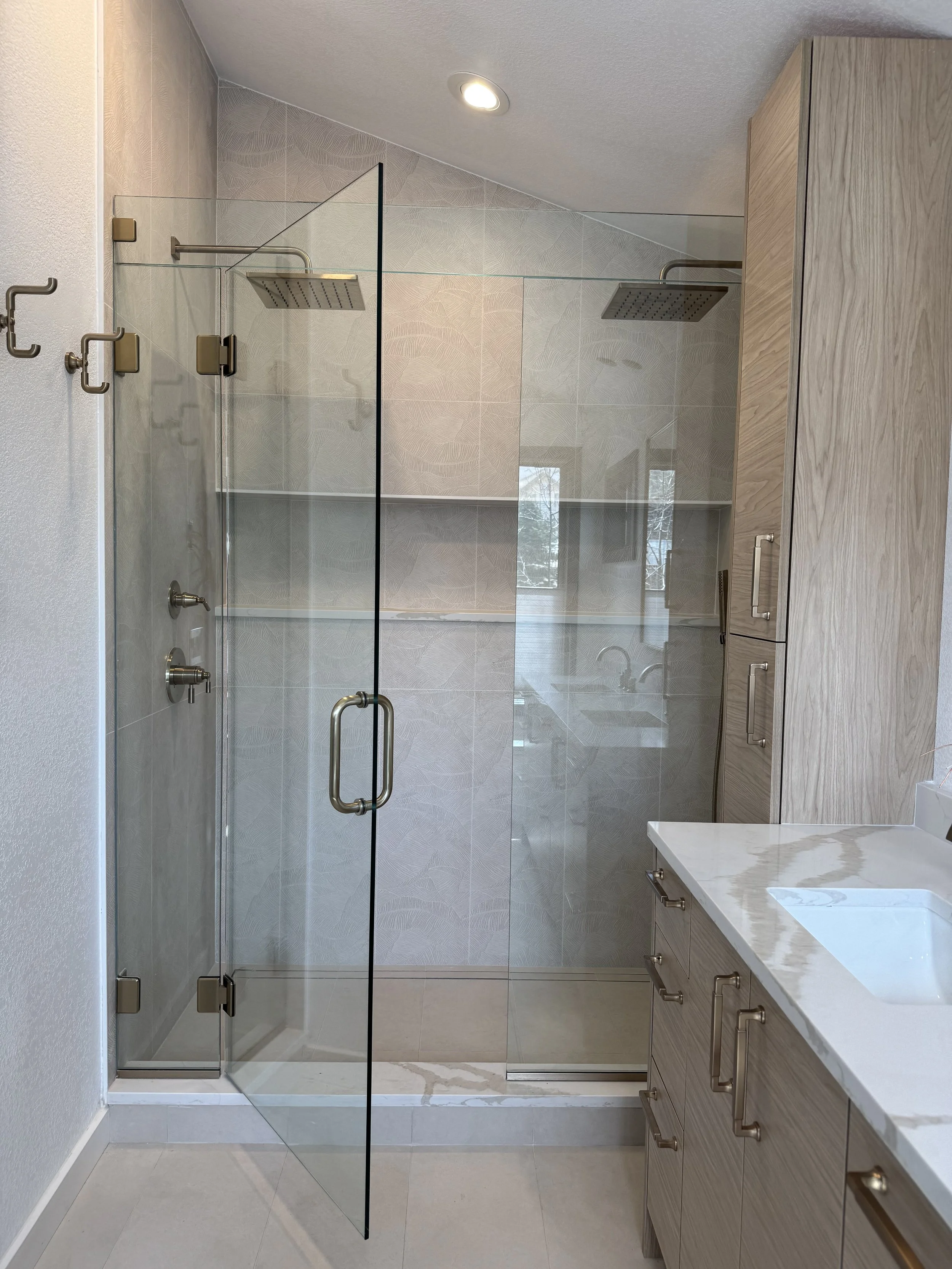 Modern bathroom with a glass shower enclosure, wooden cabinets, and a white marble countertop.