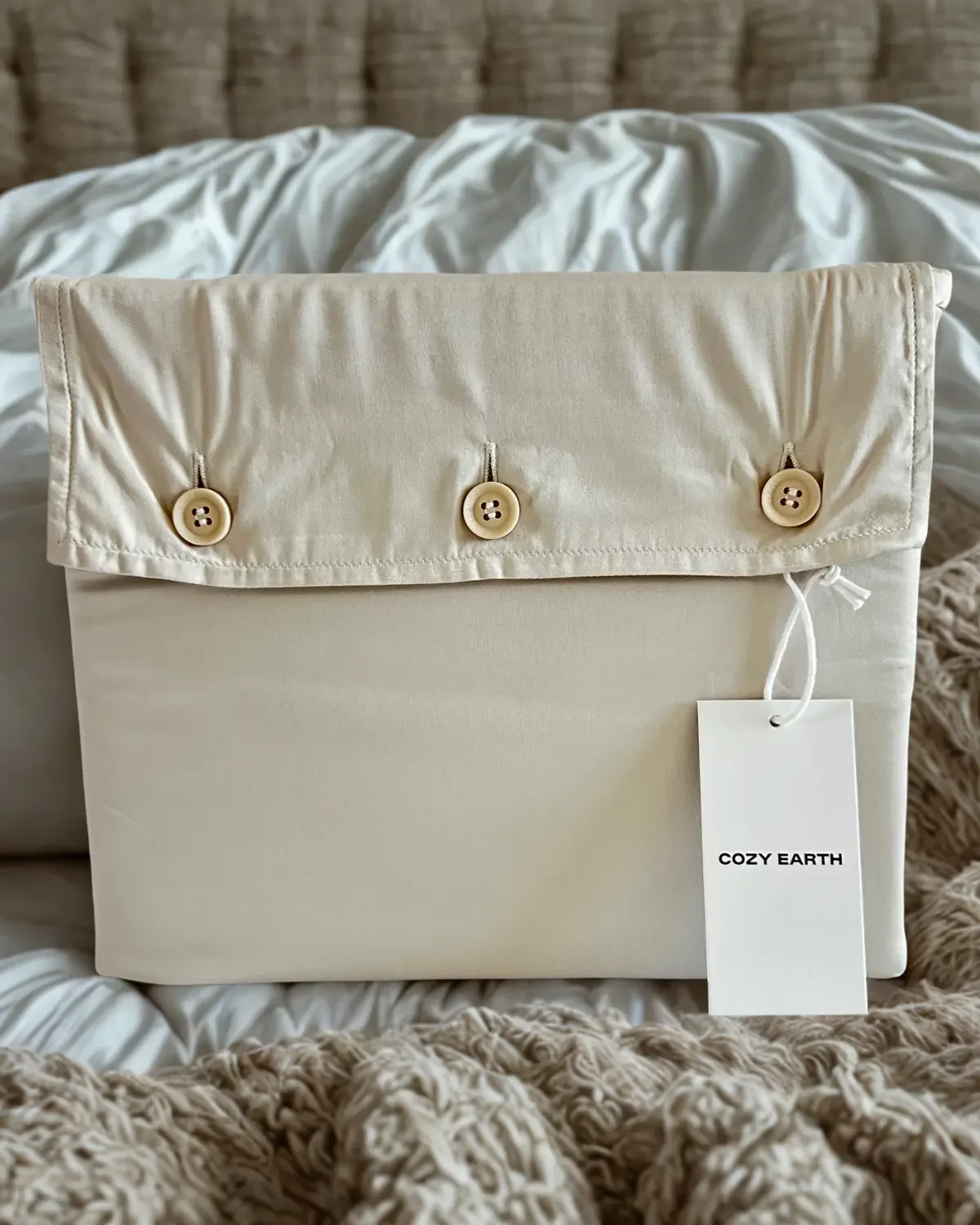 Cozy Earth sheets in fabric storage box, placed on a cozy, bed with textured blanket. A white tag with 'COZY EARTH' hangs from the box.