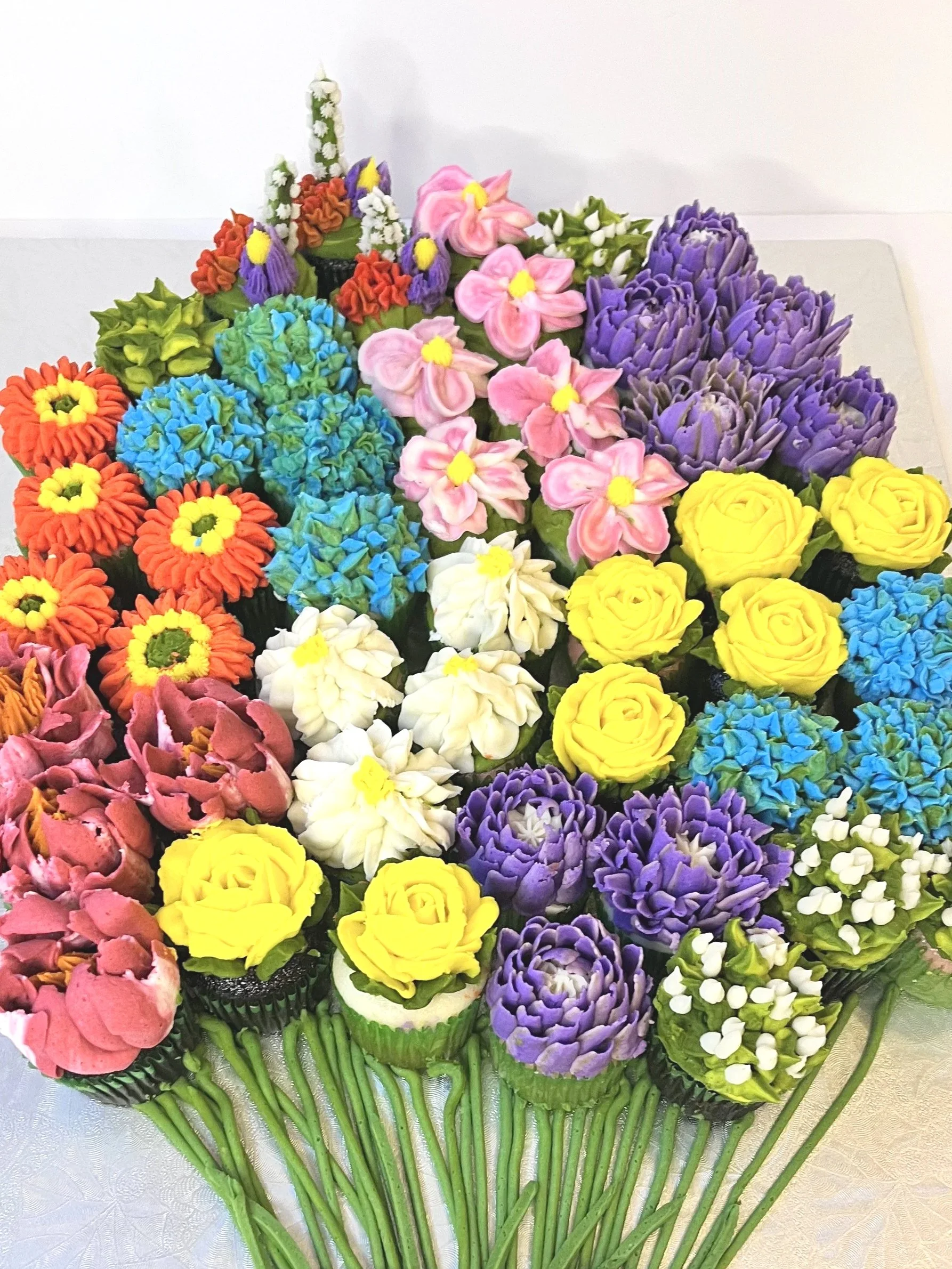 Colorful bouquet of elaborately decorated cupcakes arranged to look like a flower bouquet, tied with a pink ribbon.