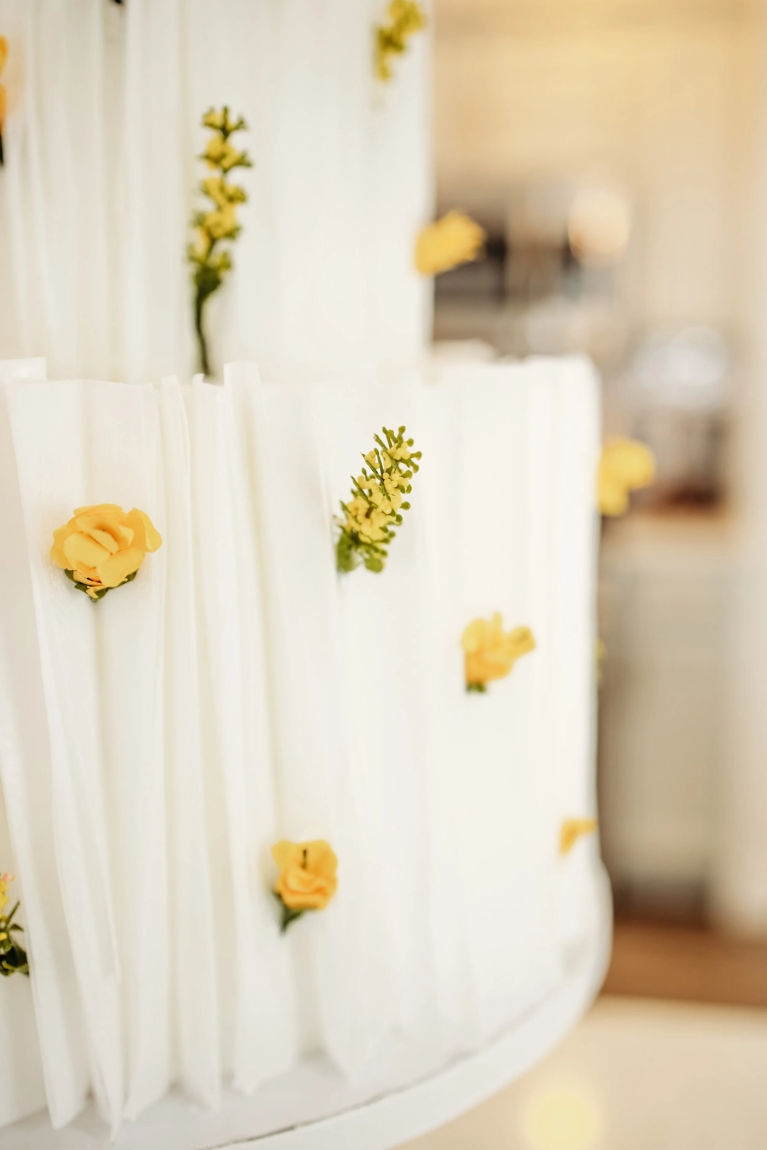 Close-up of a white tiered wedding cake decorated with small yellow flowers.