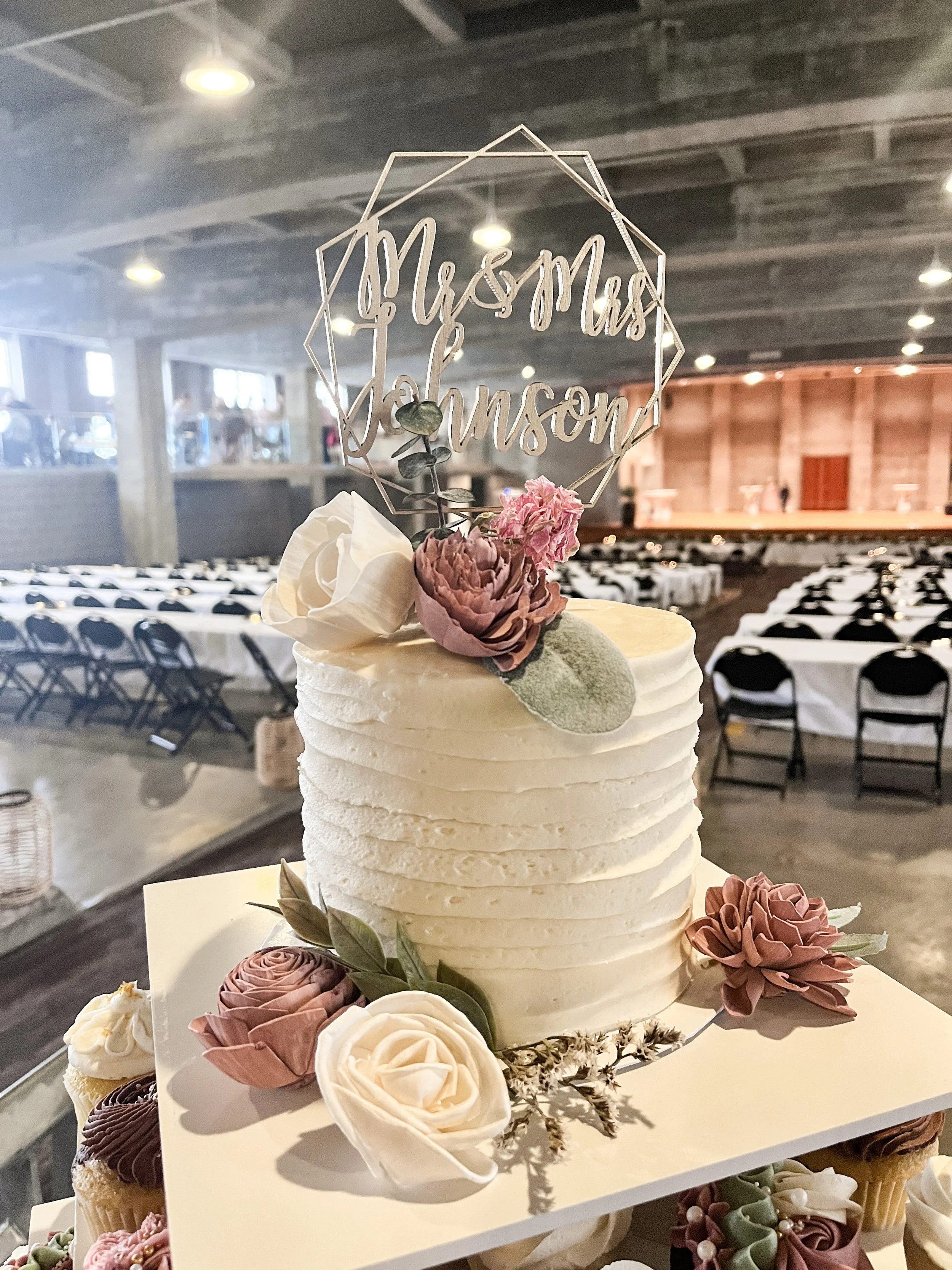 A wedding cake with white frosting, decorated with white and pink frosted flowers.