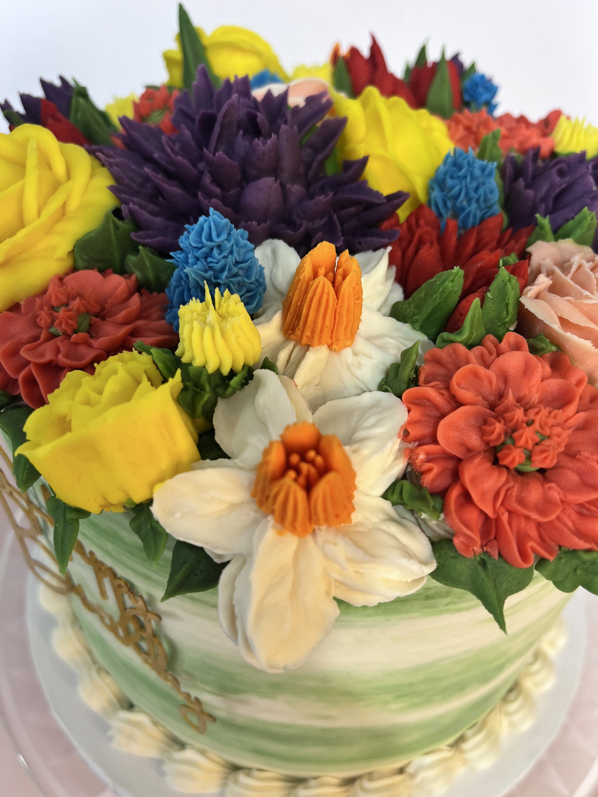 Colorfully decorated cake with various flower-shaped icing decorations in yellow, white, purple, red, orange, blue, and pink.