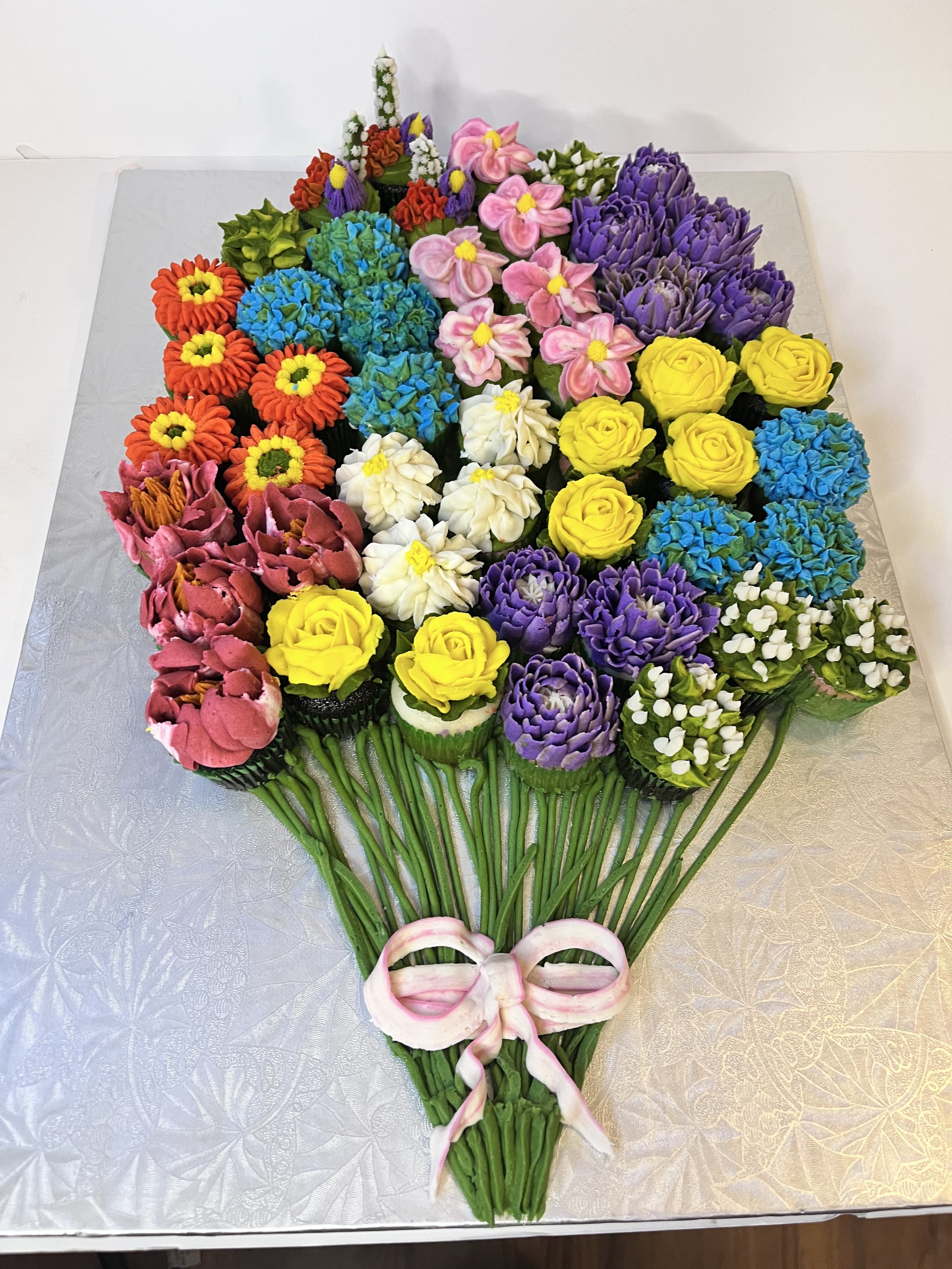 Colorful bouquet of elaborately decorated cupcakes arranged to look like a flower bouquet, tied with a pink ribbon.