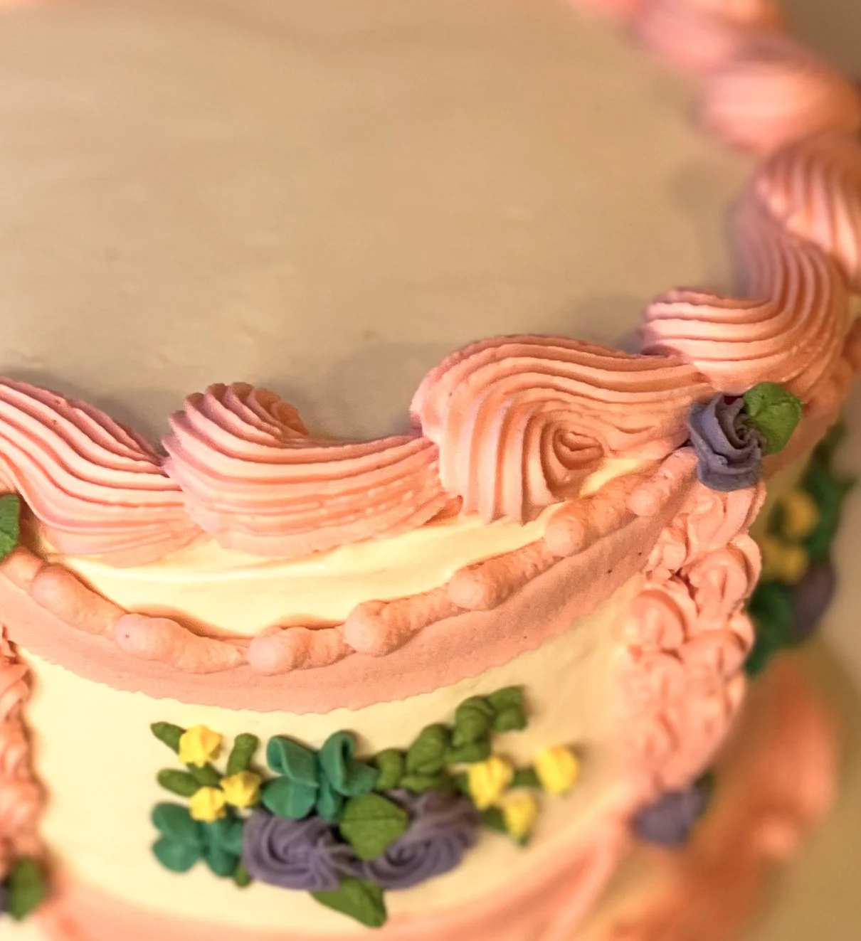 Close-up of a decorated birthday cake with pink icing, colorful floral decorations, and piped details.