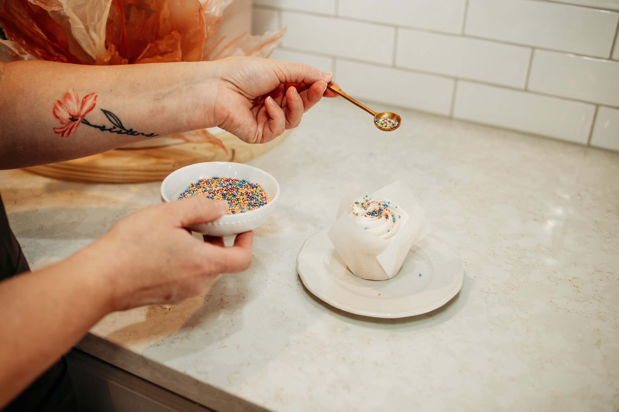 Person decorating a cupcake with colorful sprinkles in a kitchen.