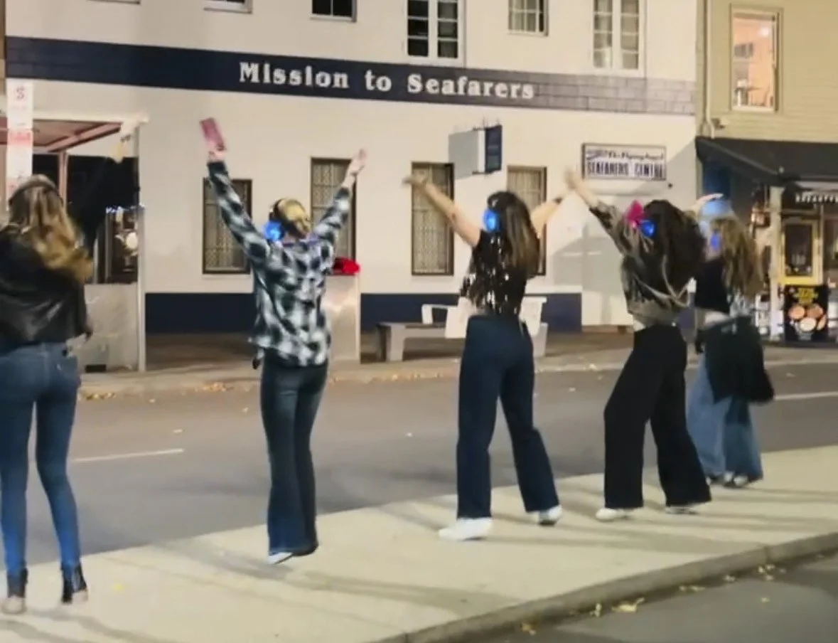 Enjoying a silent disco walking tour in Hobart. 5 women dancing in the street with their heaphones on.