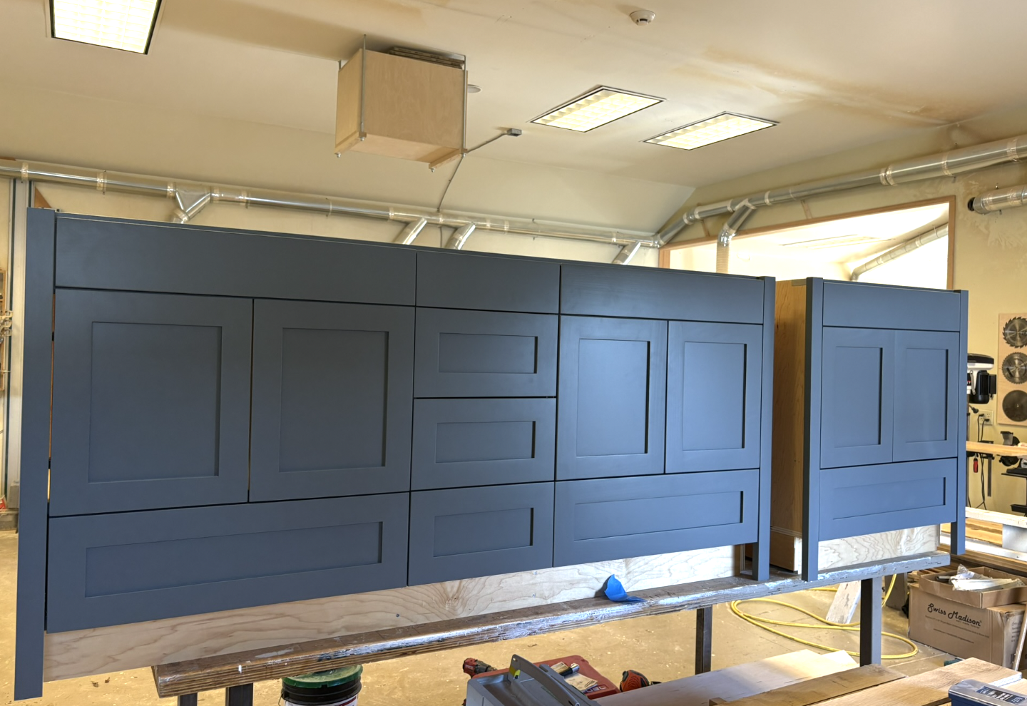 Handcrafted blue kitchen cabinets in progress in a woodworking shop, mounted on a workbench.