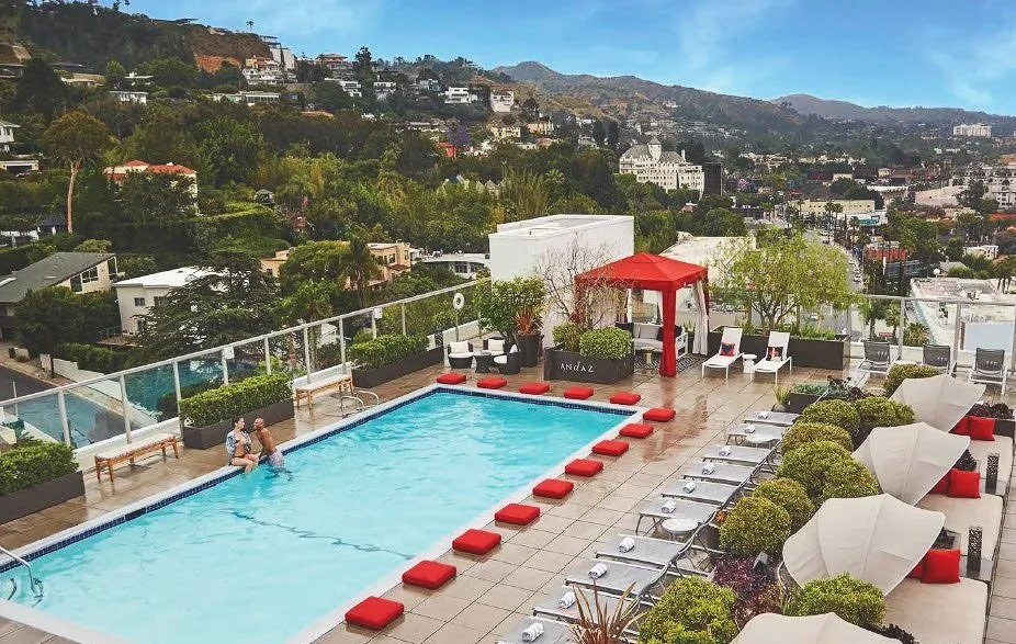 Rooftop swimming pool with lounge chairs, umbrellas, and city view in the background.