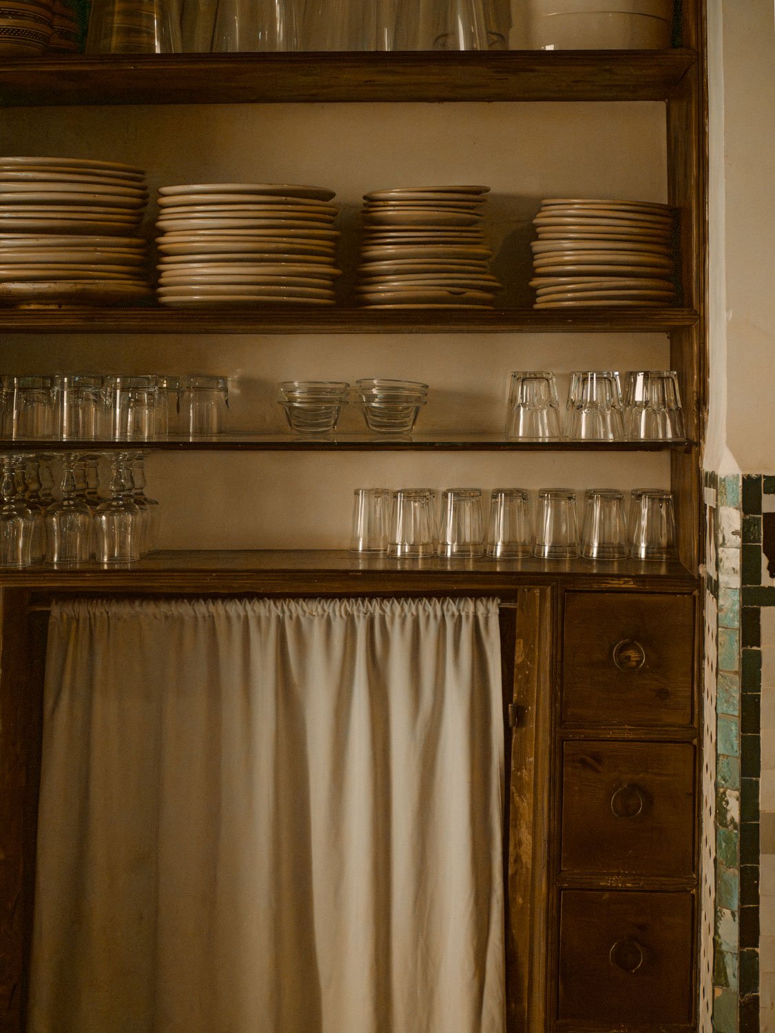 Traditional Moroccan kitchen with zellige tilework and aged wooden furniture, lit by soft natural light.