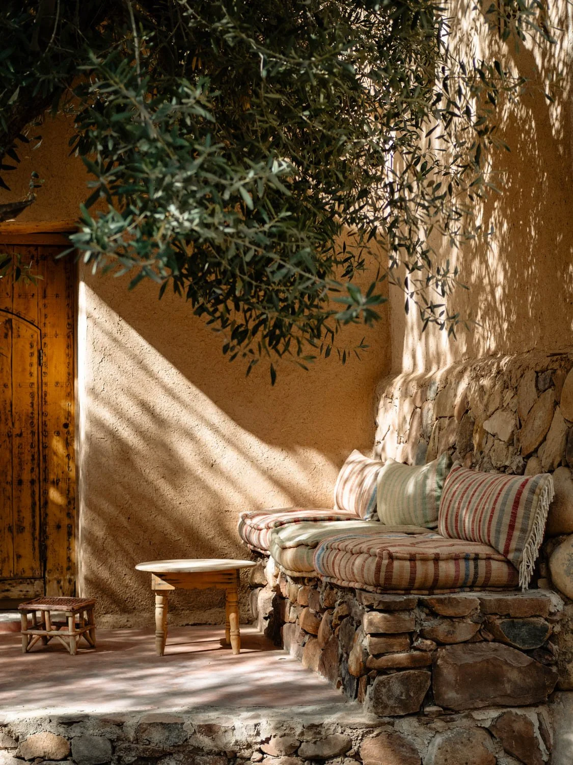 Shaded bench at Berber Lodge near Marrakech, layered Moroccan textiles in the garden