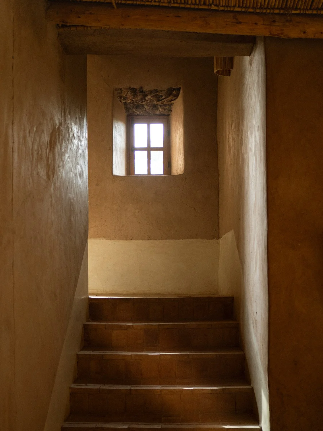 Main house interior at Berber Lodge near Marrakech, earthen-toned staircase and window light at the end of the space