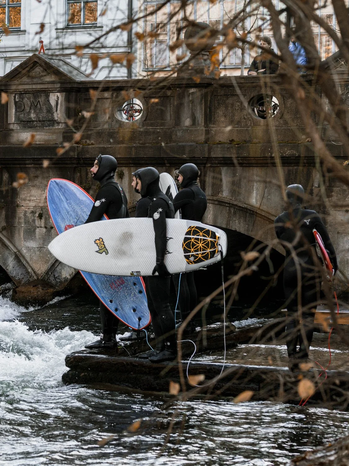 Surfers waiting at the Eisbachwelle river wave on a winter day, Munich, Germany
