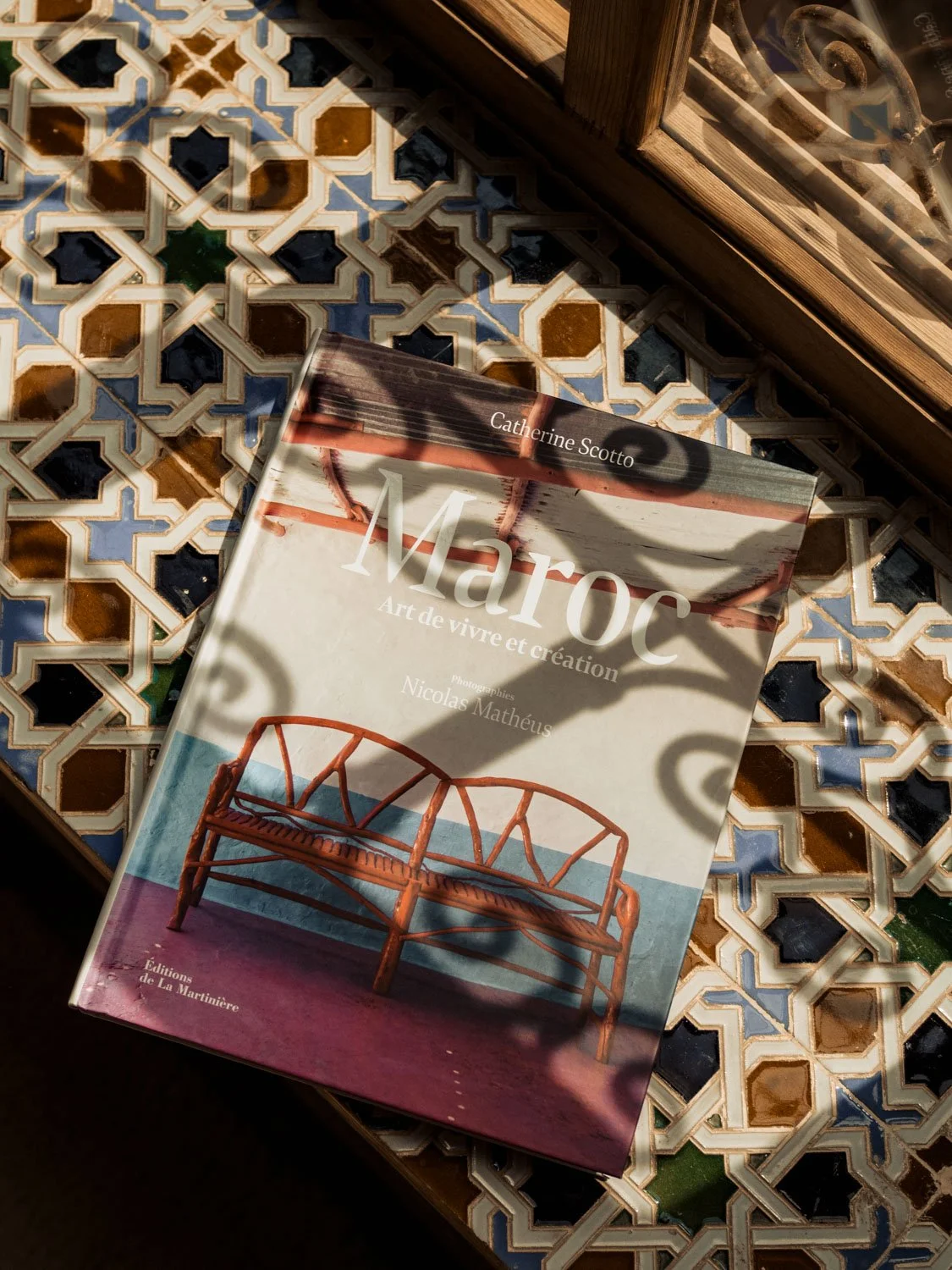 Interior detail at Berber Lodge near Marrakech, book on Moroccan architecture resting on colorful traditional tiles in sunlight