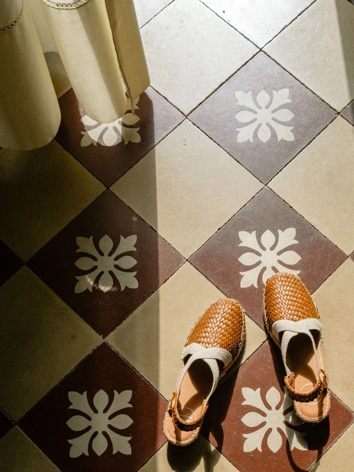 Patterned tiles in an old Sicilian villa seen from above, with espadrilles placed on the floor under soft morning light.
