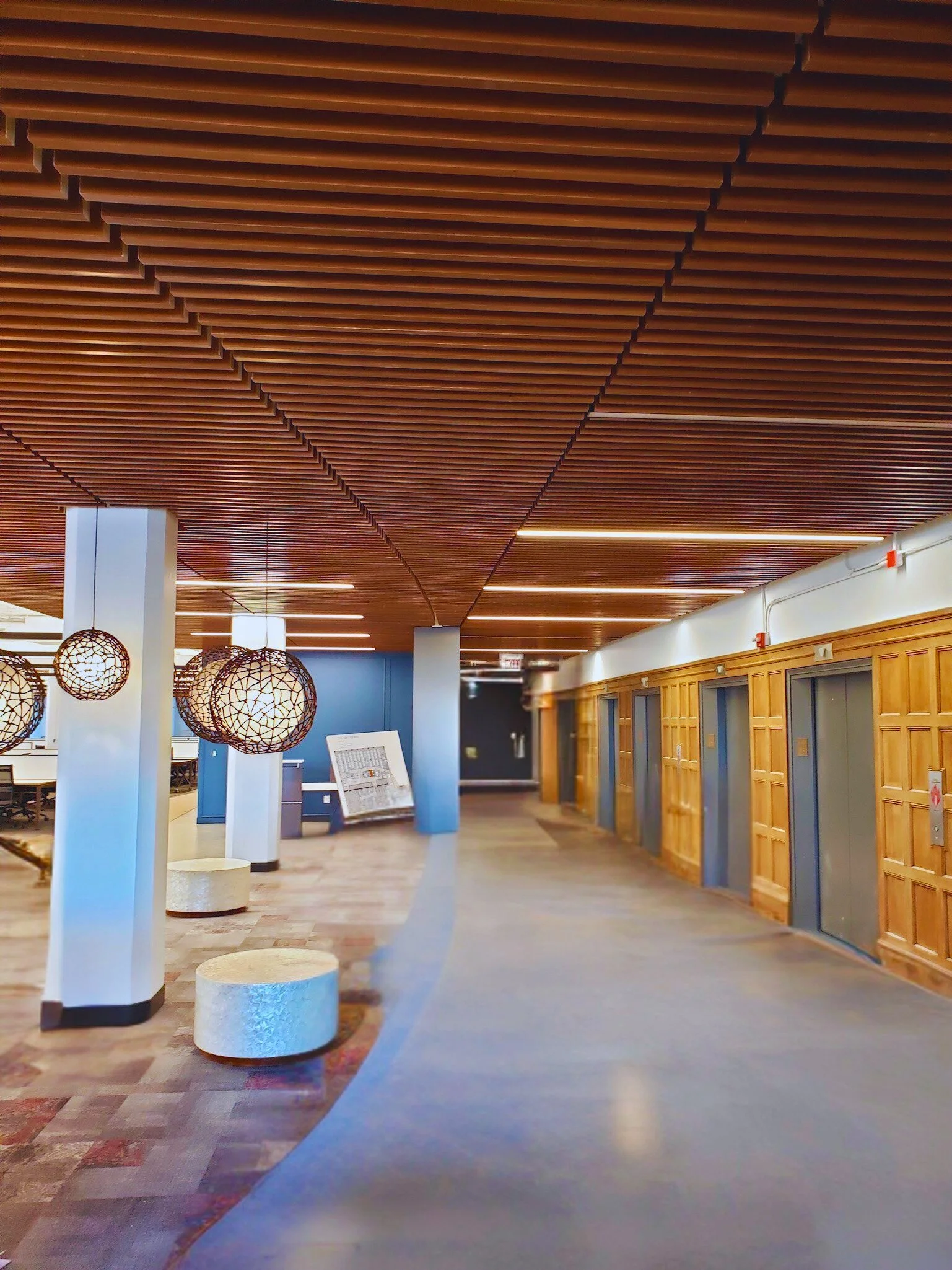 Interior of an elevator lobby with wooden wall paneling, blue walls, decorative hanging light fixtures, and multiple elevator doors.