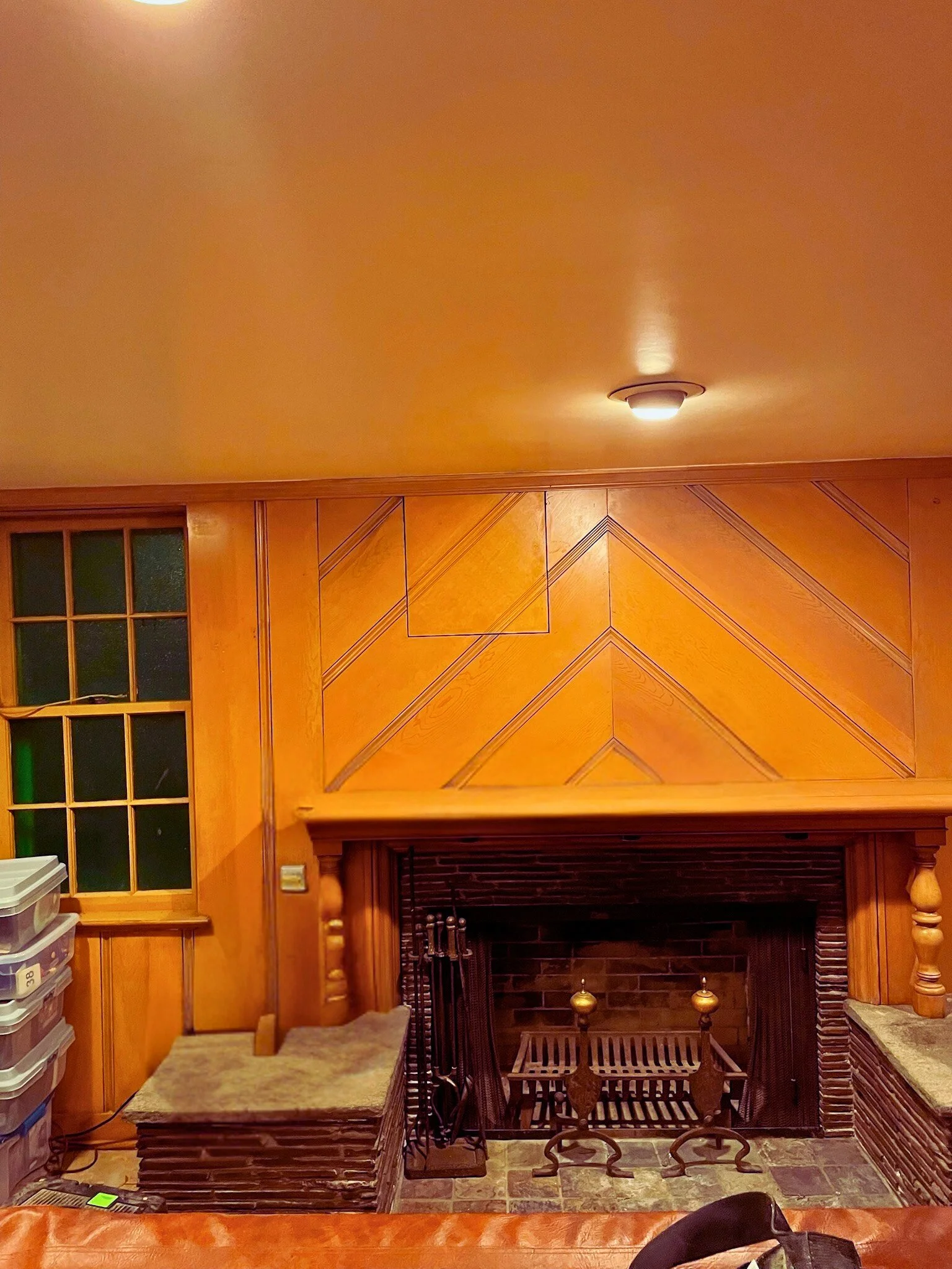 Living room with wooden paneling on the fireplace and wall, a window with multiple panes, and a ceiling light fixture.