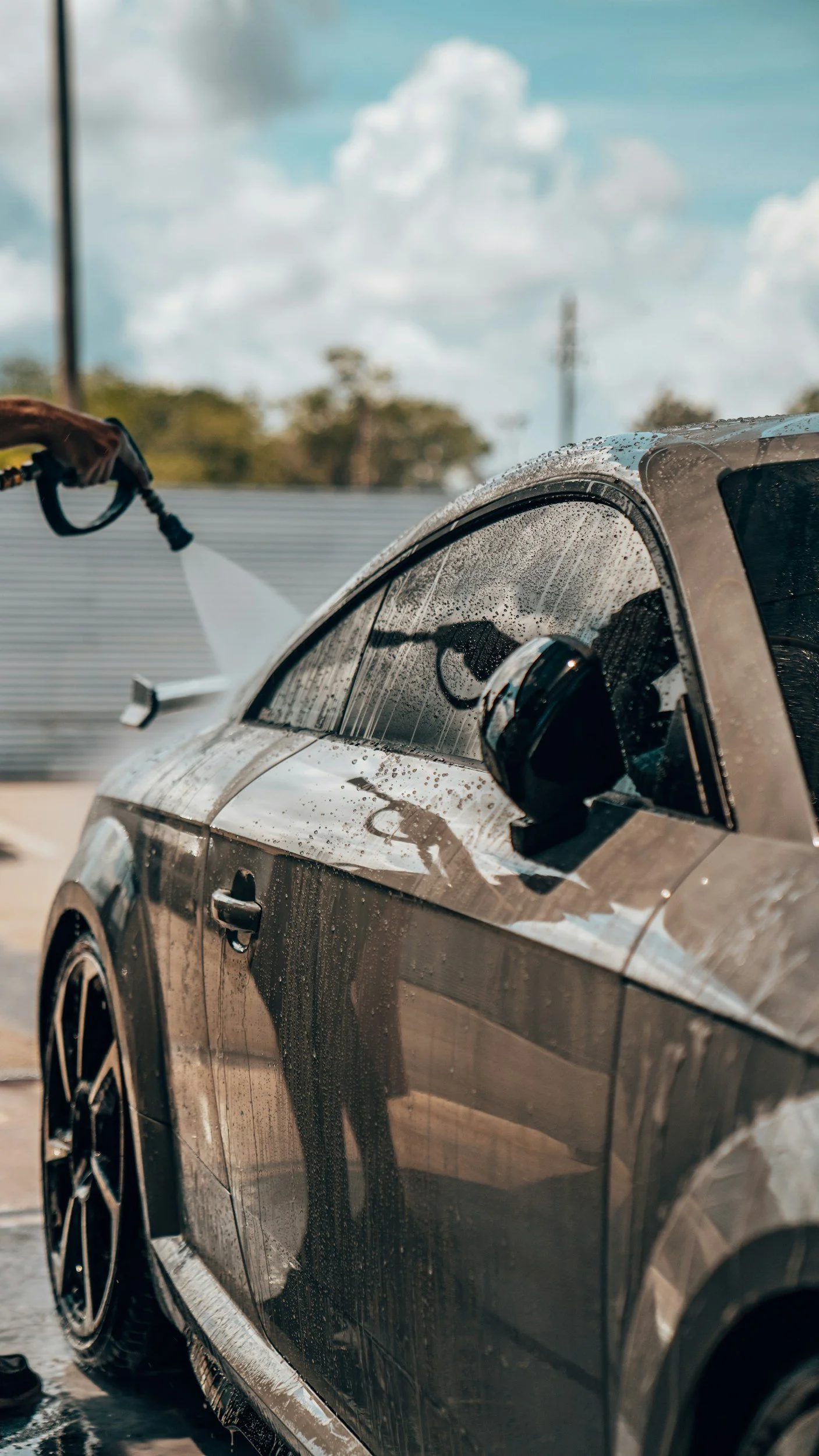Person spraying water on a black car during a car wash.