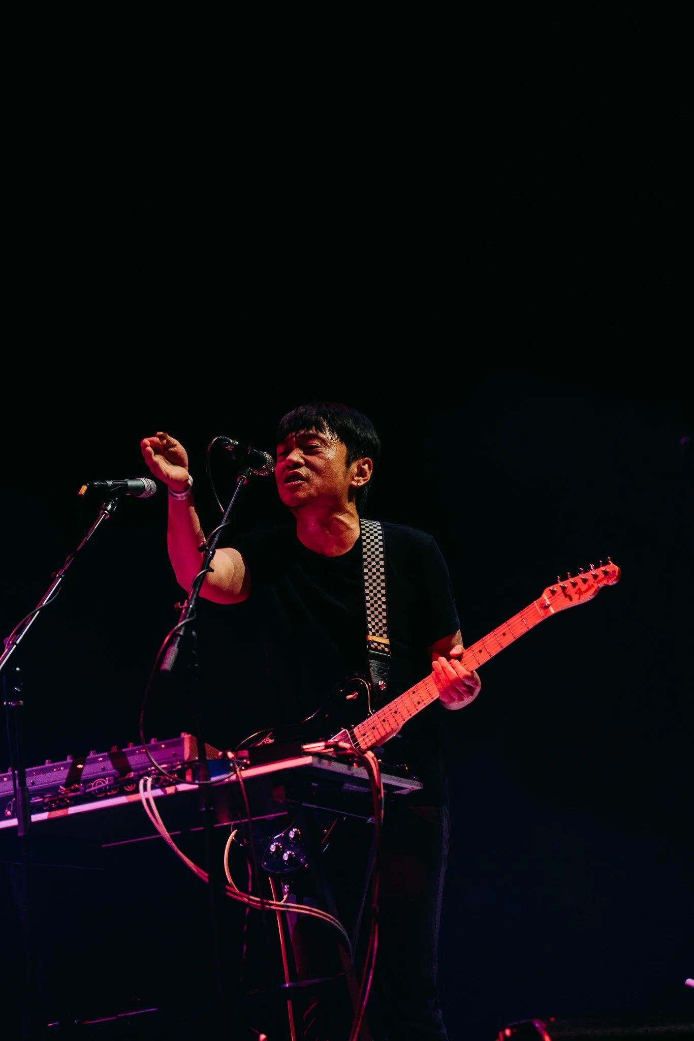 A musician performs on stage with a guitar, singing into a microphone, under dark lighting