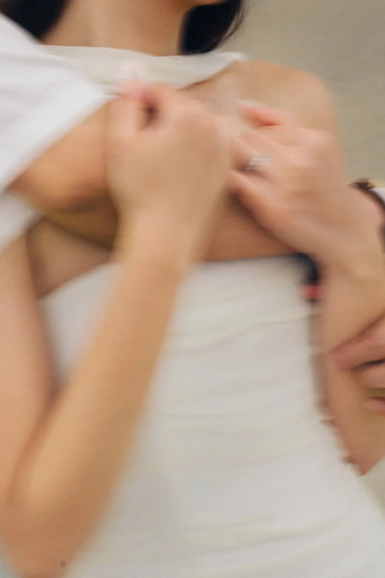 A person is receiving a shoulder massage, with hands on their shoulder, wearing a white tank top.