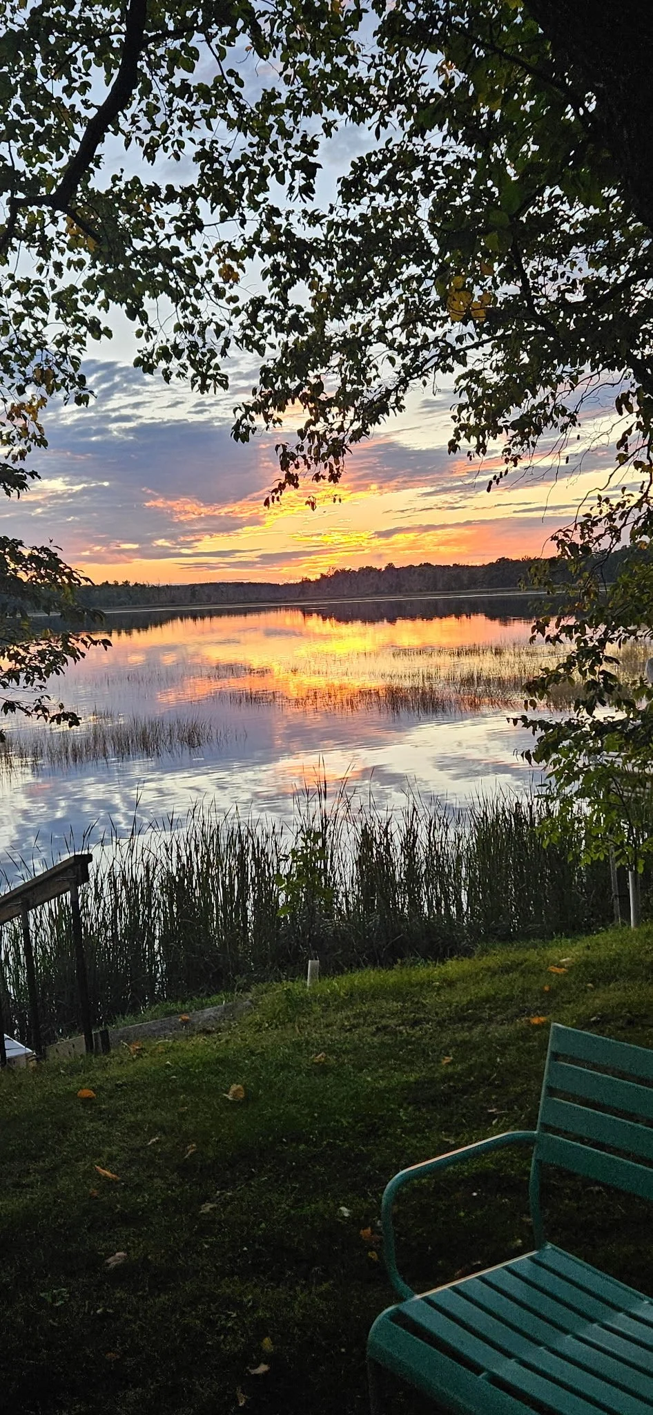 Pink and orange sunset reflected across the lake beside a small dock.