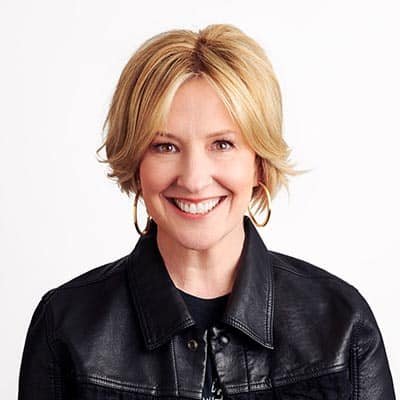 Portrait of a smiling woman with short blonde hair, wearing a black leather jacket.