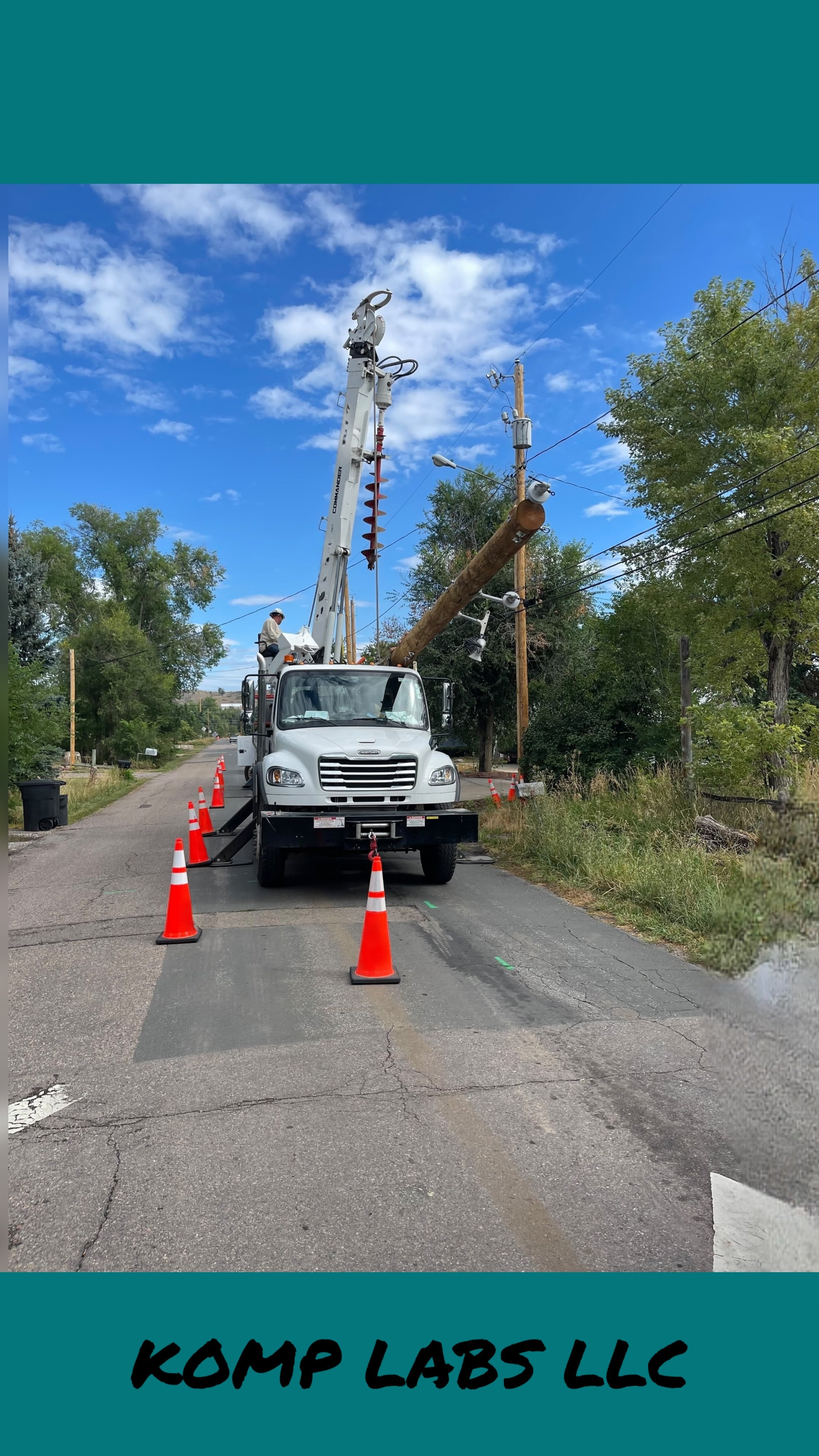 A utility truck with a crane lifting a fallen utility pole with wires, working on repairing power lines, surrounded by orange traffic cones on a rural street.