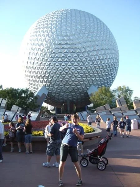 People in front of Spaceship Earth at EPCOT, a large geodesic sphere with a patterned surface, in Disney World.